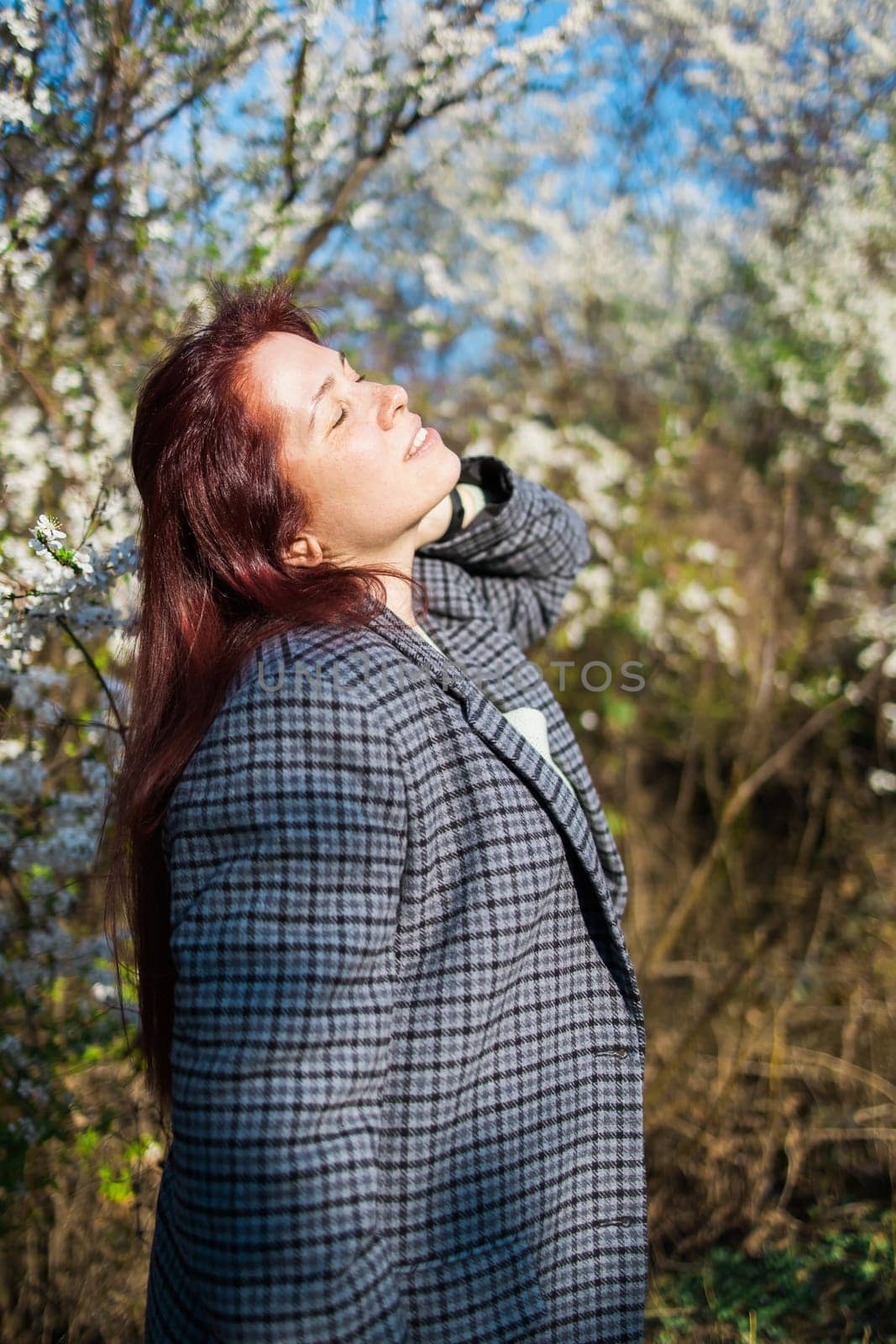 Beautiful red-haired woman enjoying smell in a flowering blooming spring garden. Spring blossom. by Satura86