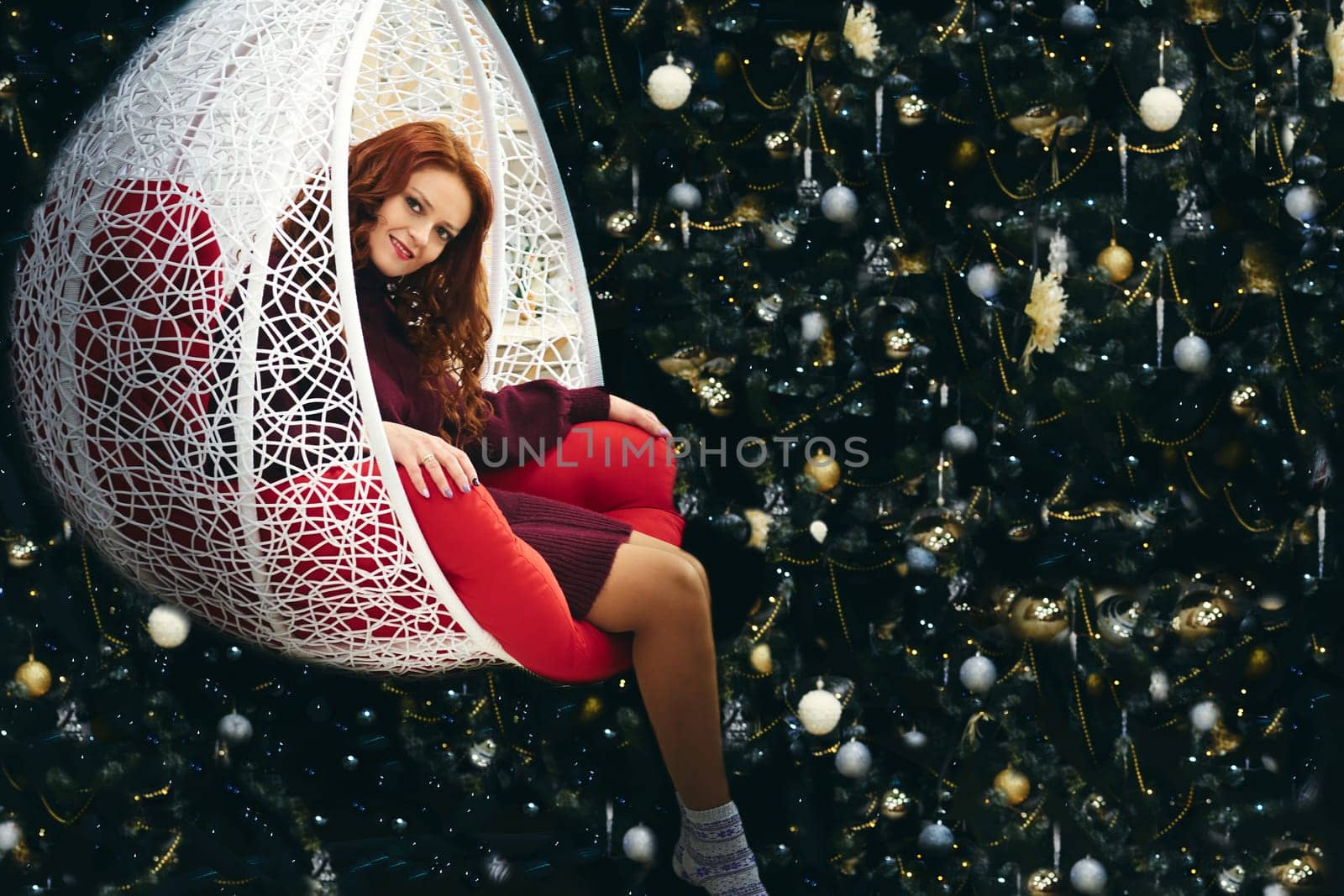 a chair mounted on rockers or springs, so as to rock back and forth. Young pretty woman in a wicker rocking chair near the New Year tree.