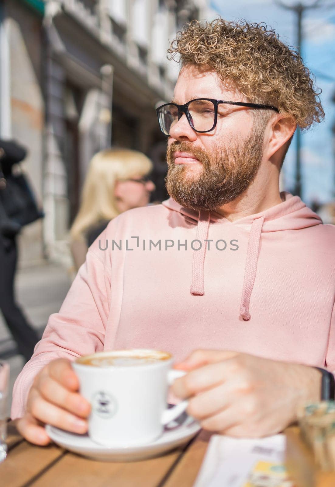 Millennial bearded man having breakfast at table of street cafe on spring day, drinking warm cappuccino. Spring restaurant terrace by Satura86