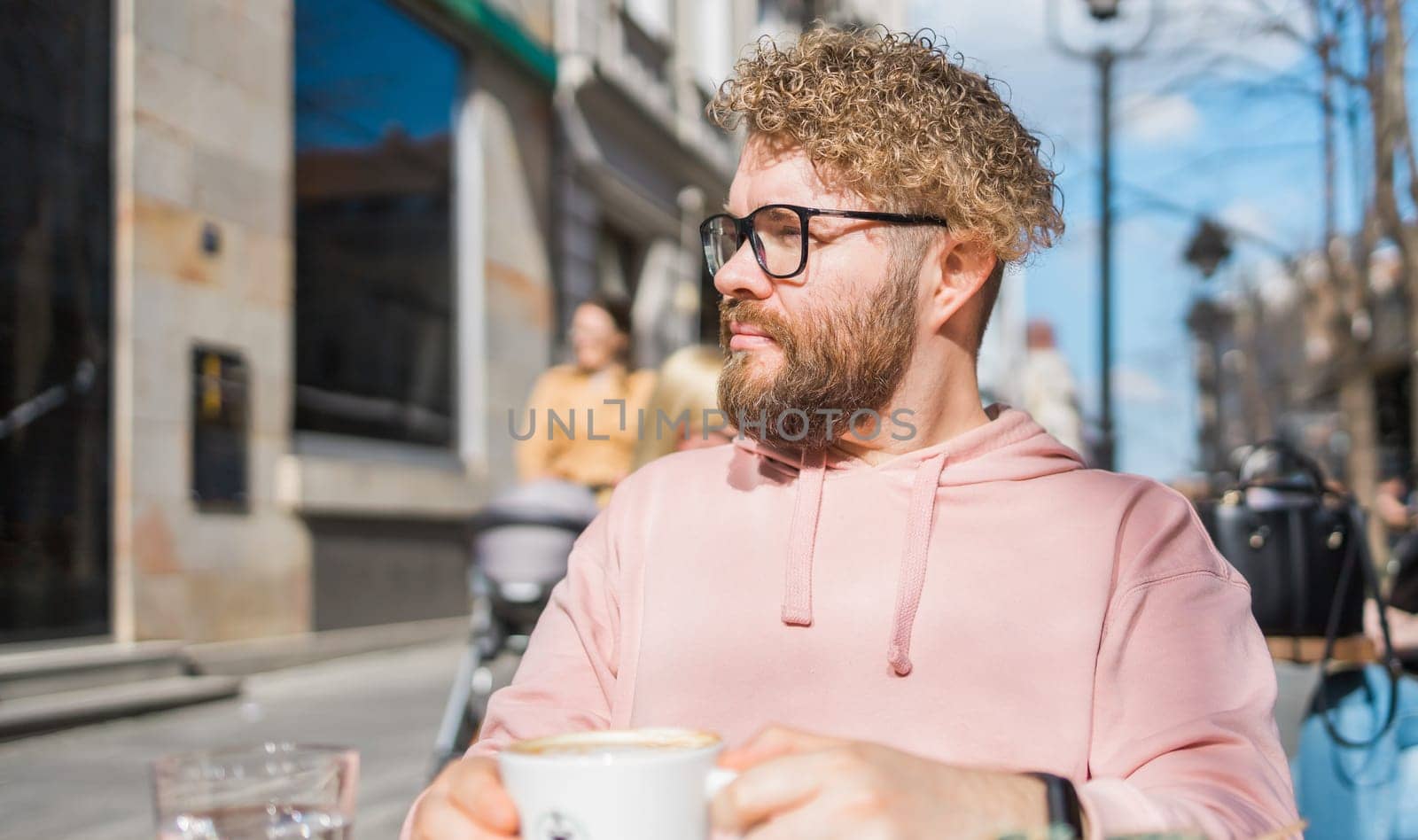 Millennial bearded man having breakfast at table of street cafe on spring day, drinking warm cappuccino. Spring restaurant terrace.