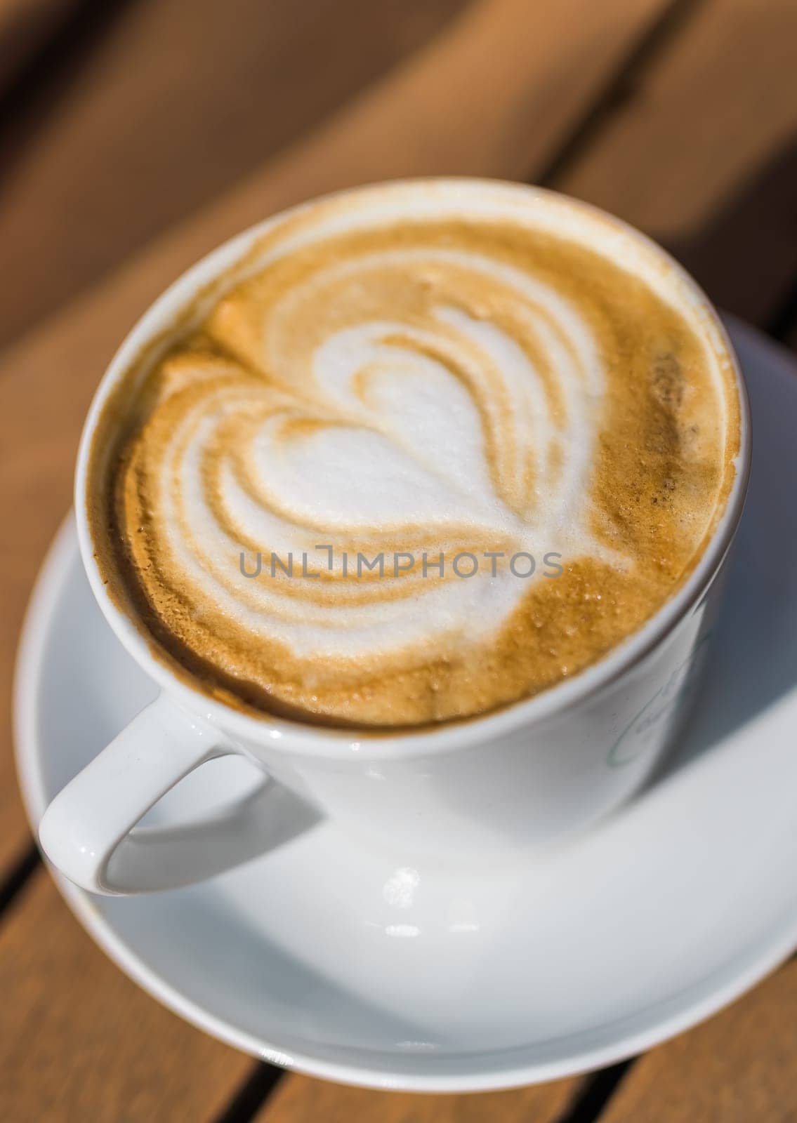 Coffee on wooden background. Cup of cappuccino with latte art on brown table with sunbeam. Fresh morning coffee with delicious milk foam
