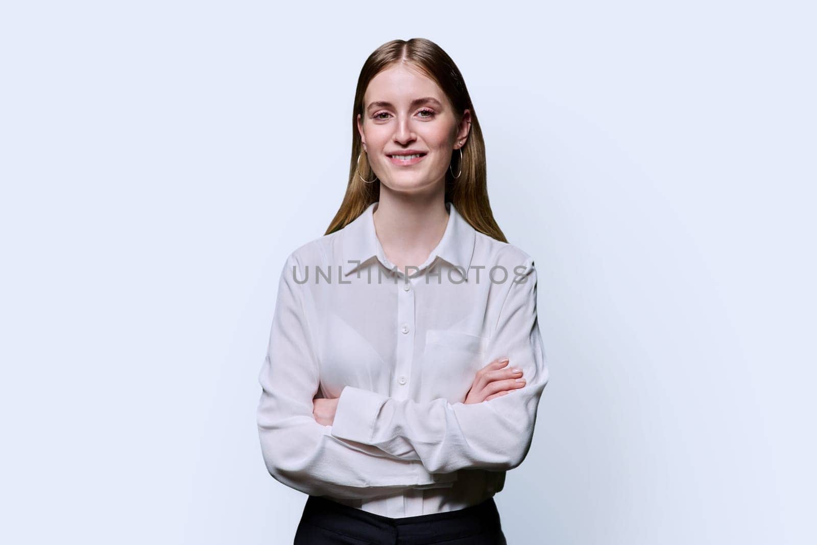 Portrait of young teenage smiling female in white shirt with crossed arms on white studio background. Confident beautiful happy college student girl looking at camera