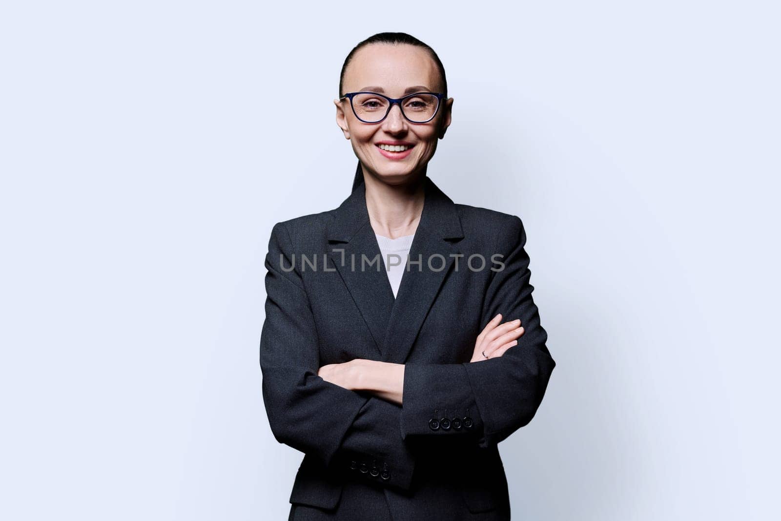 Portrait of happy smiling with teeth business woman in 30s with crossed arms, on white studio background. Confident female in glasses, suit looking at camera. Business work job career people concept