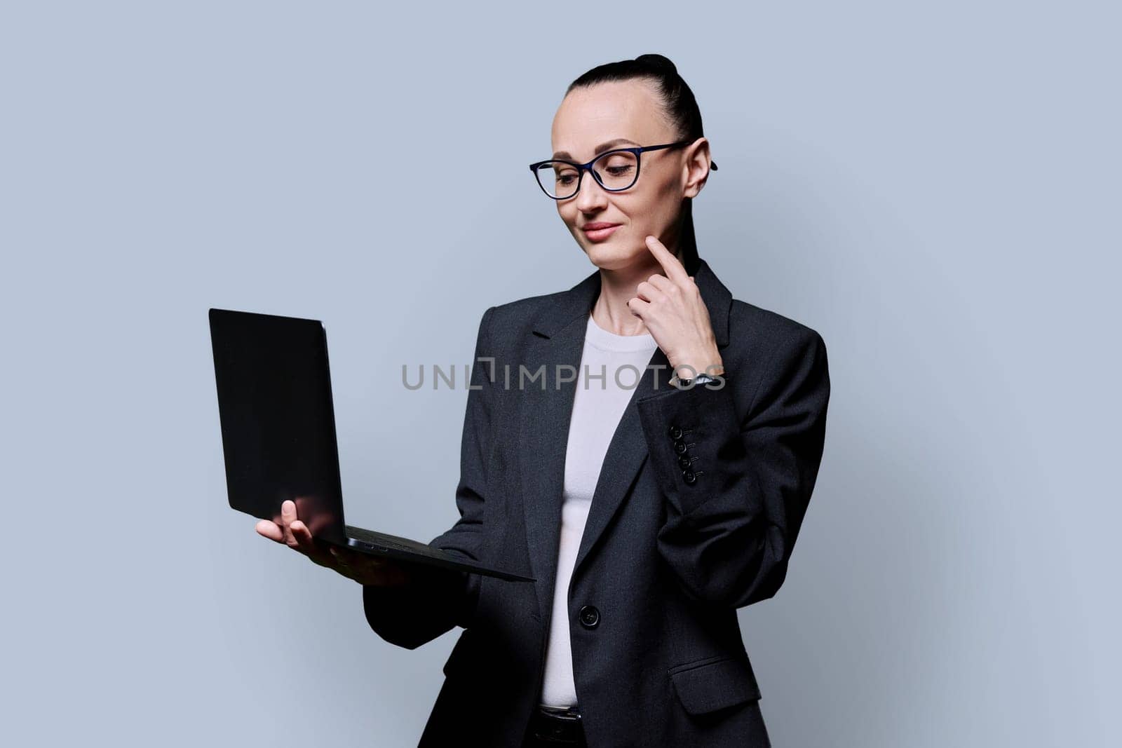 Middle-aged business confident woman using laptop on gray background by VH-studio