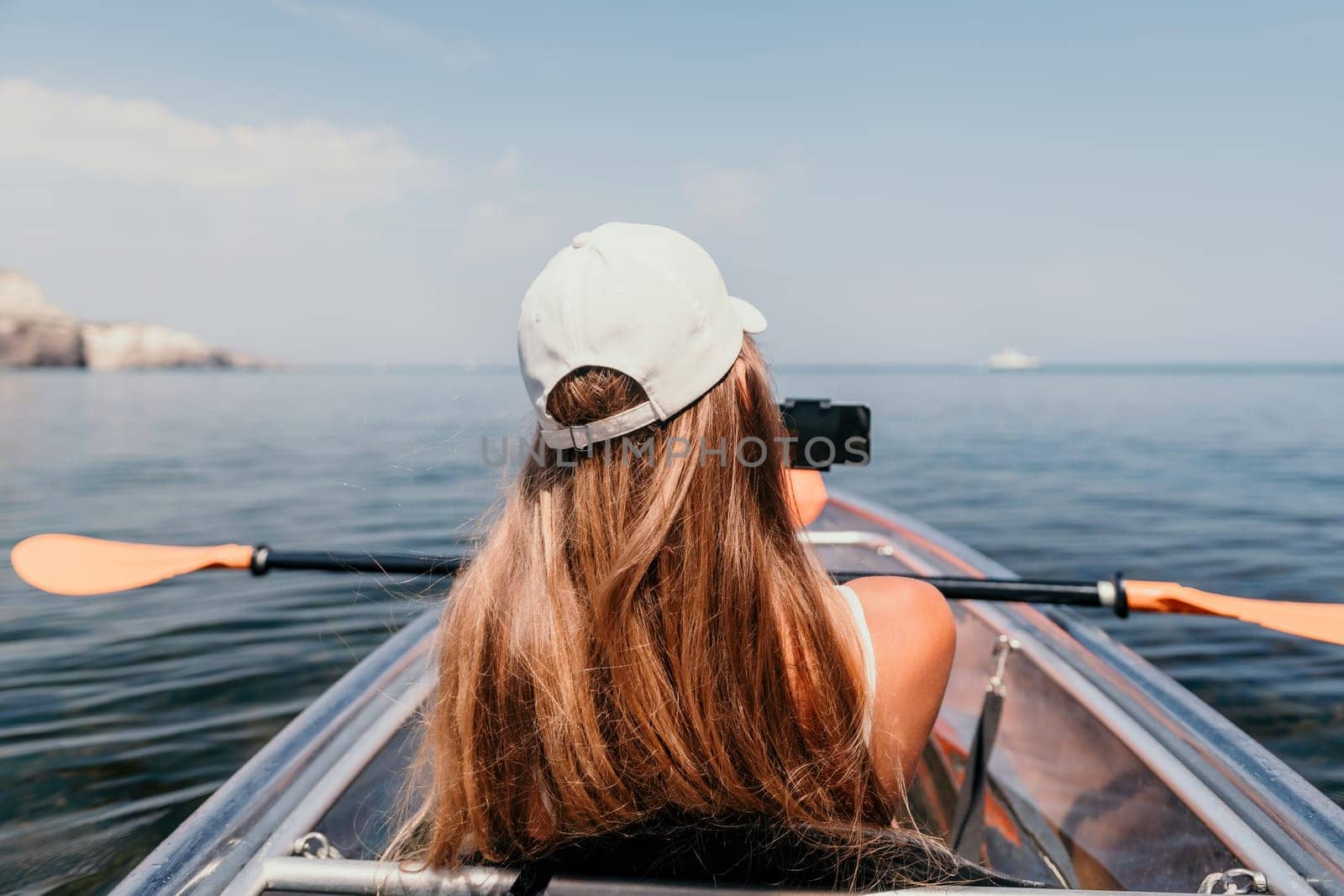 Woman in kayak back view. Happy young woman with long hair floating in transparent kayak on the crystal clear sea. Summer holiday vacation and cheerful female people having fun on the boat.