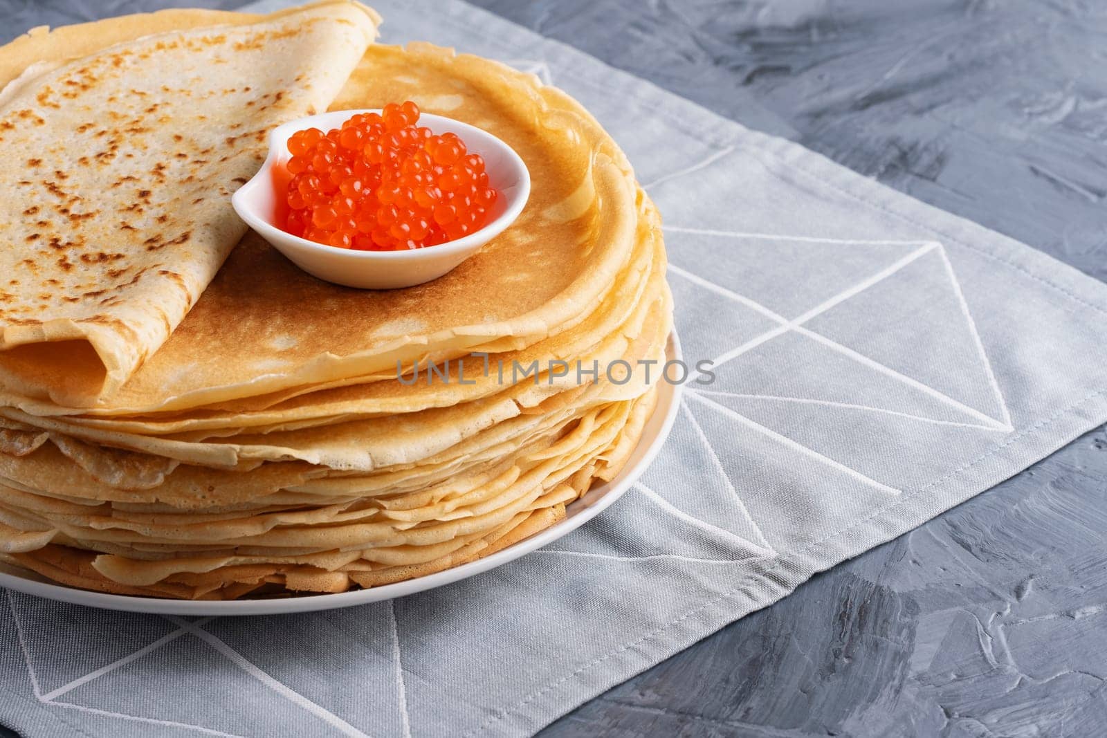 Pancakes with red caviar on grey background, with copy space for text,