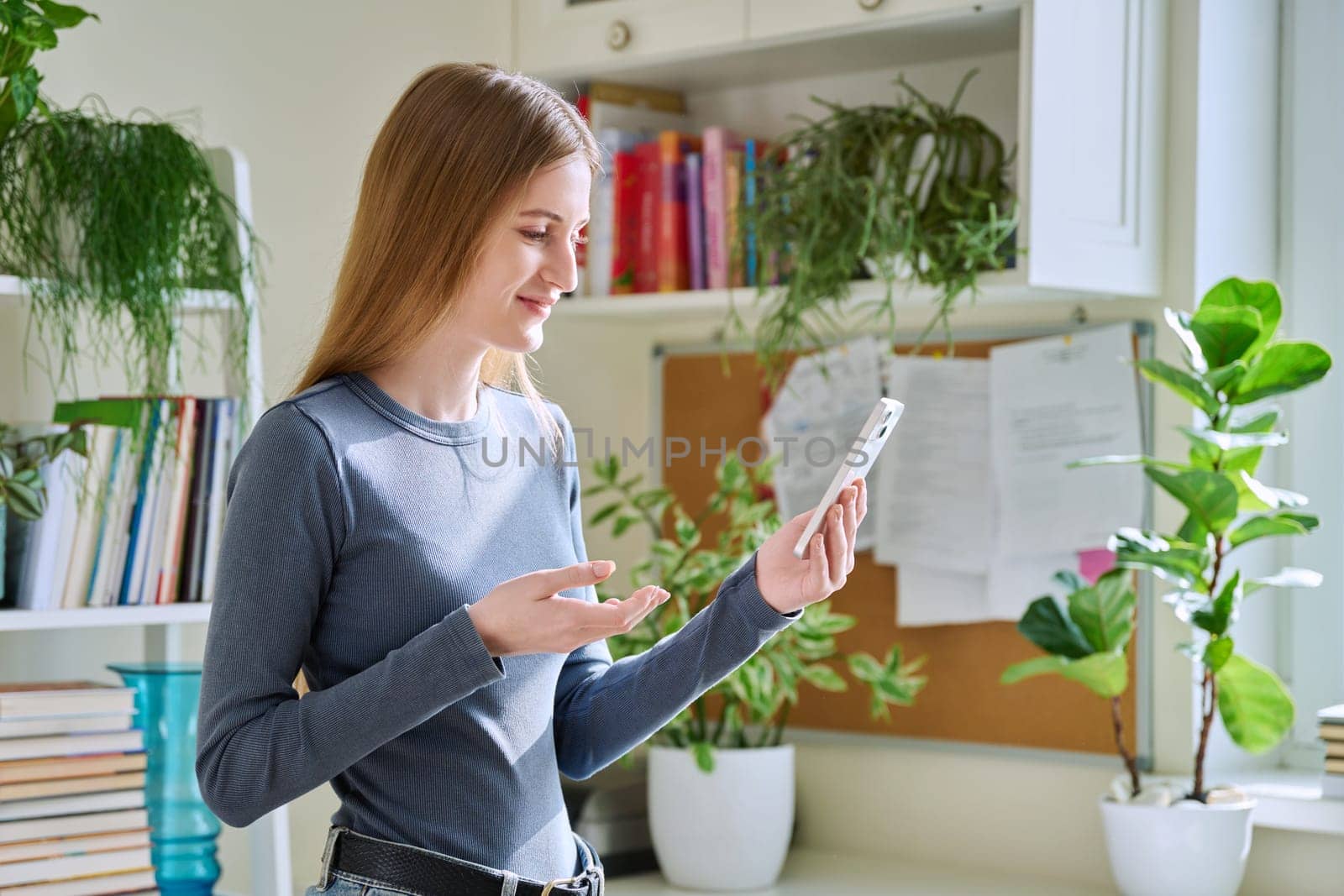 Young teenage female using smartphone for video conversation, home interior. Talking teenage girl looking at the phone screen, online video chat conference call. Technology, communication, leisure
