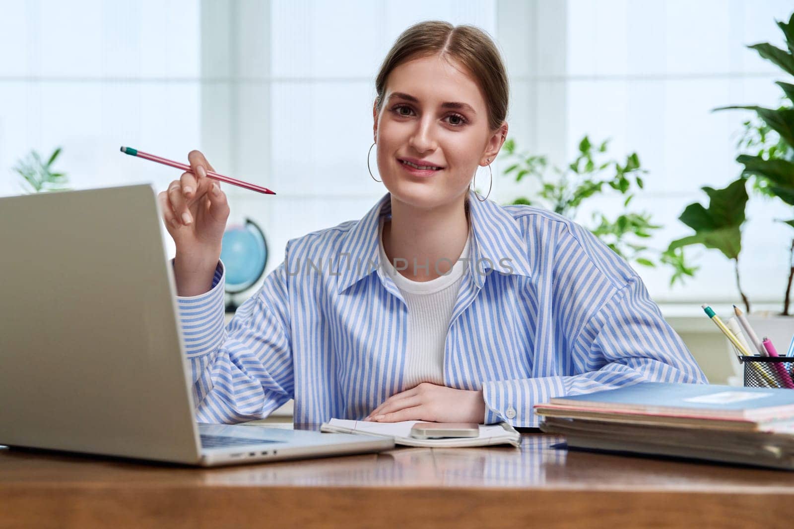 Portrait of high school, college student smiling young female sitting at desk with laptop computer looking at camera. Education, training, e-learning, 16,17,18 year old youth