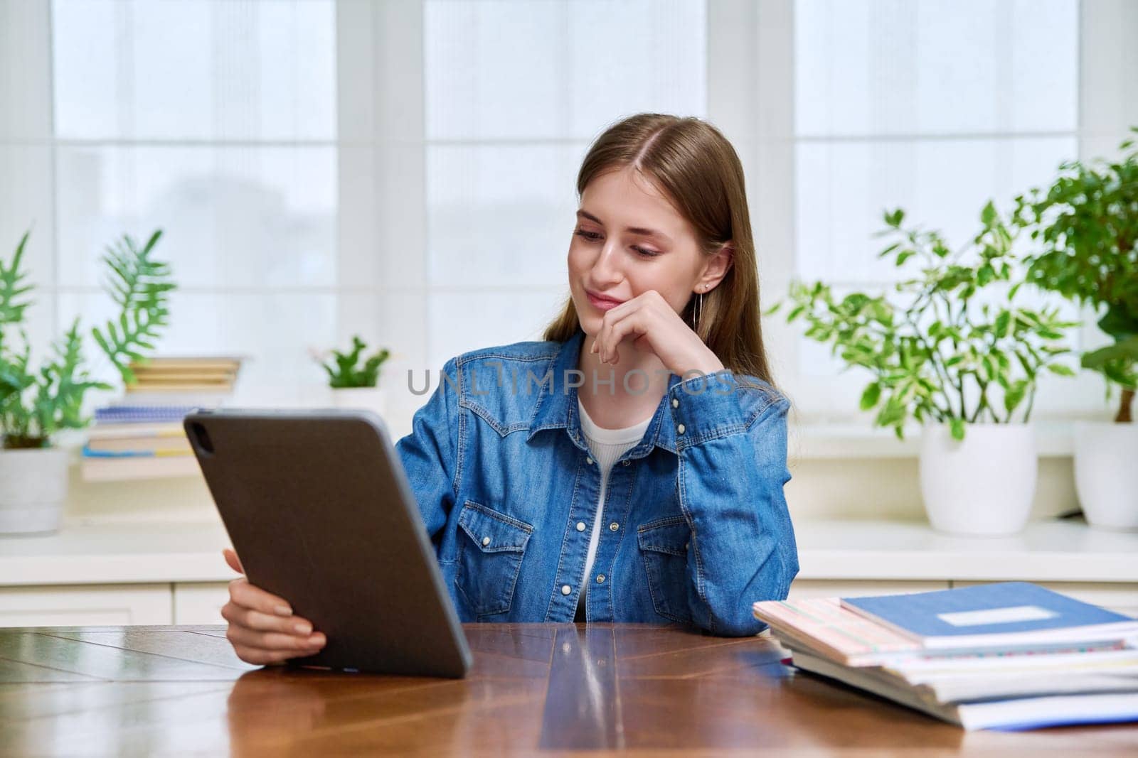 Young teenage female student sitting at home looking talking in web camera of digital tablet. Girl teenager 16,17,18 years old studying remotely, video conference call, e-learning technology education