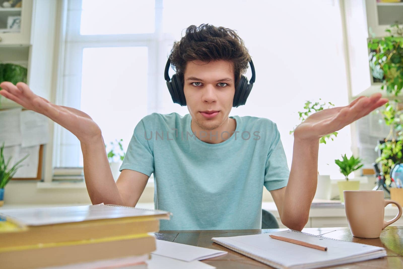 Webcam view of college student guy wearing headphones, talking looking at camera, sitting at desk in home. Young male studying online, video chat call conference, e-learning technology education