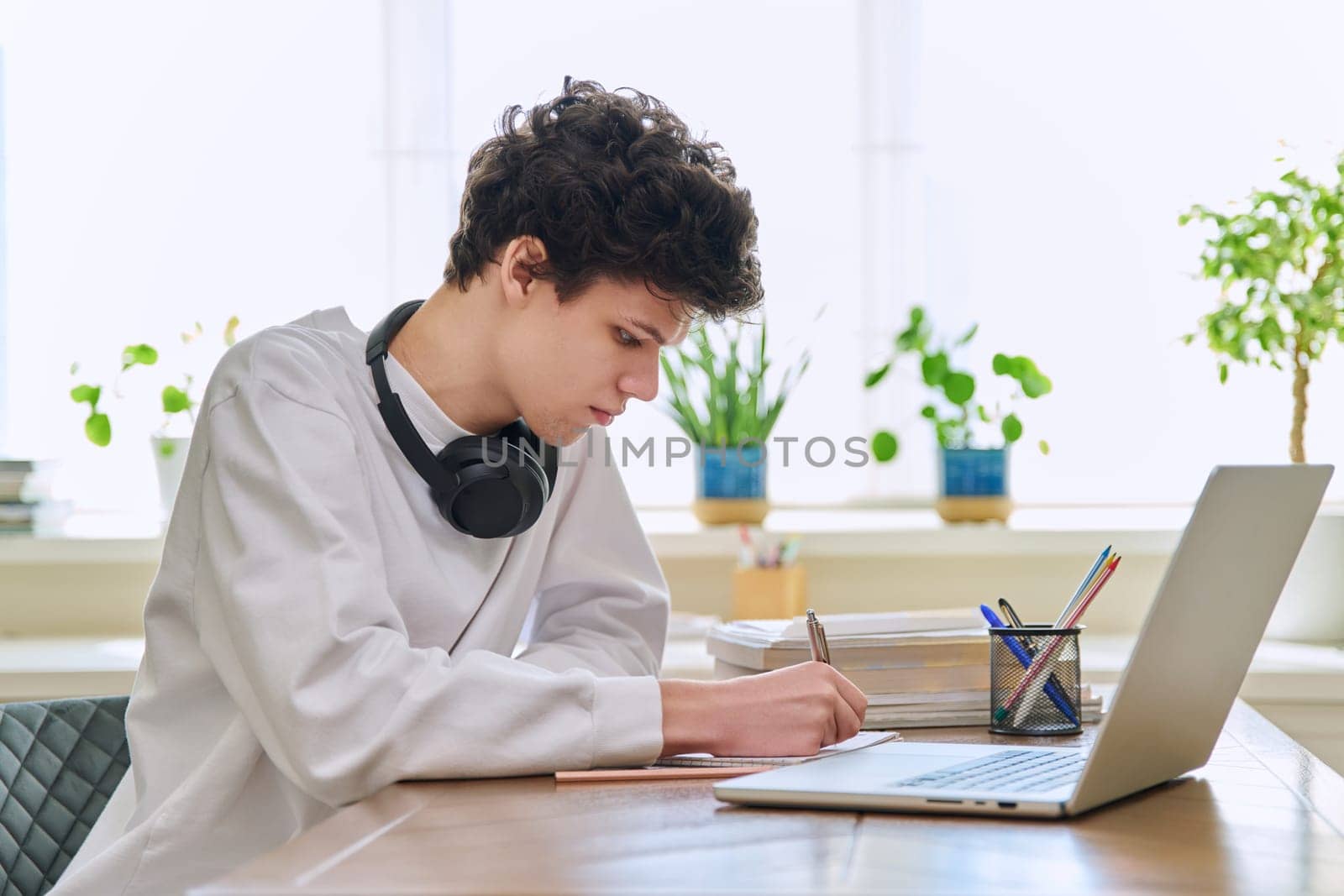 Young male college student sitting at desk at home using laptop. Guy 19-20 years old studying at home, using a computer for education leisure communication