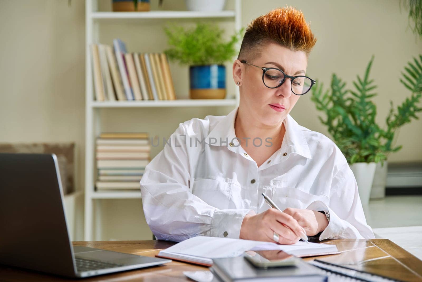 Middle aged woman working with computer papers, remote workplace in home office by VH-studio