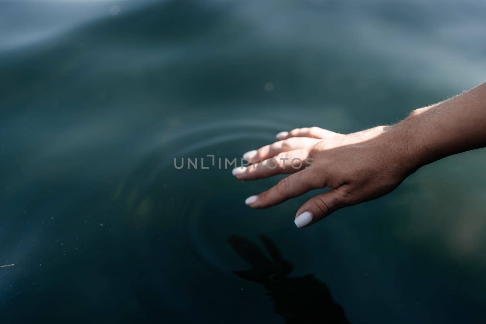 The hand touches the water, creating ripples. The water is calm and clear, and the hand is white. Concept of tranquility and peacefulness. by Matiunina