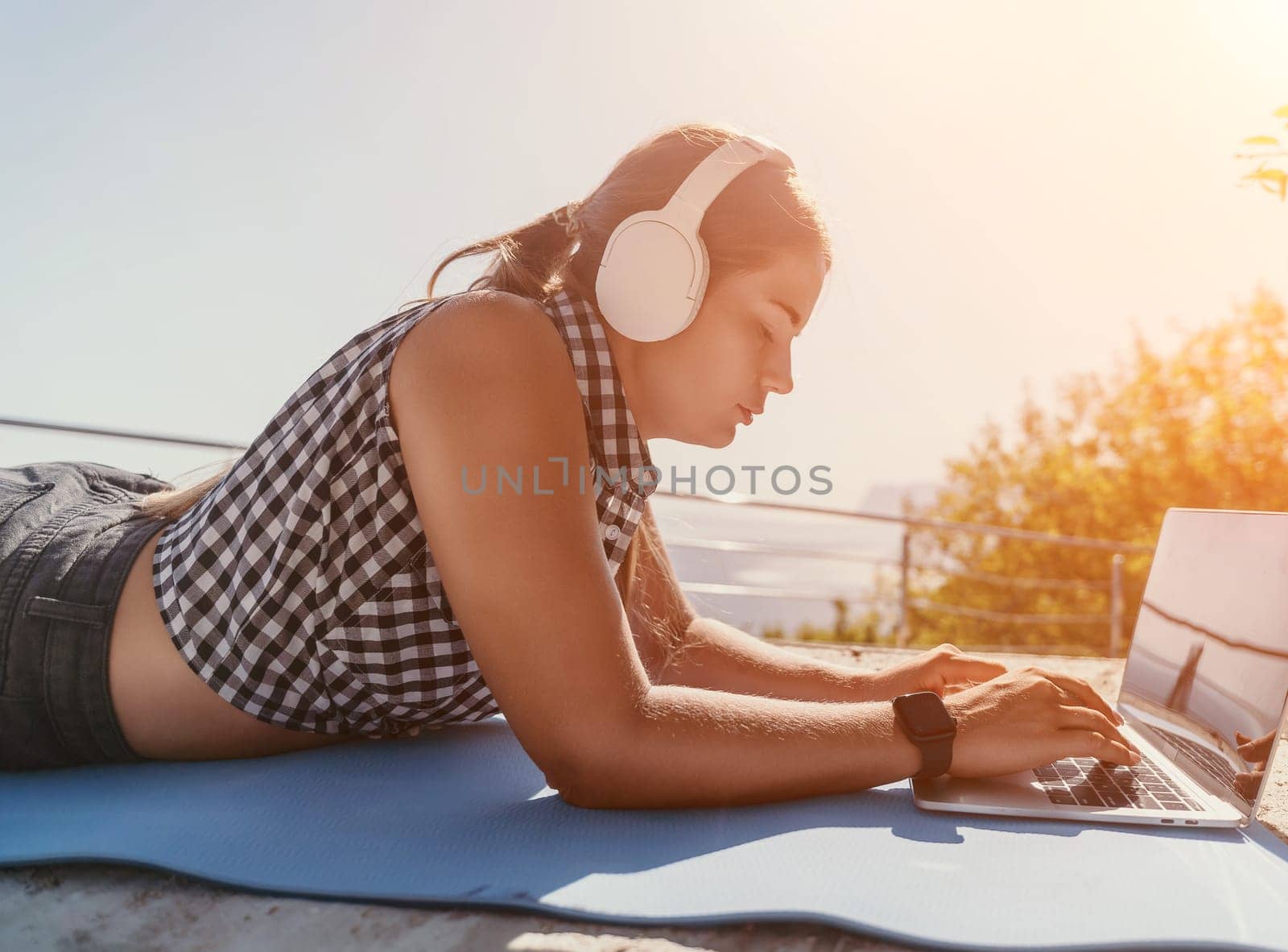 Woman laptop sea. Working remotely on seashore. Happy successful woman female freelancer working on laptop by the sea at sunset, makes a business transaction online. Freelance, remote work on vacation by panophotograph