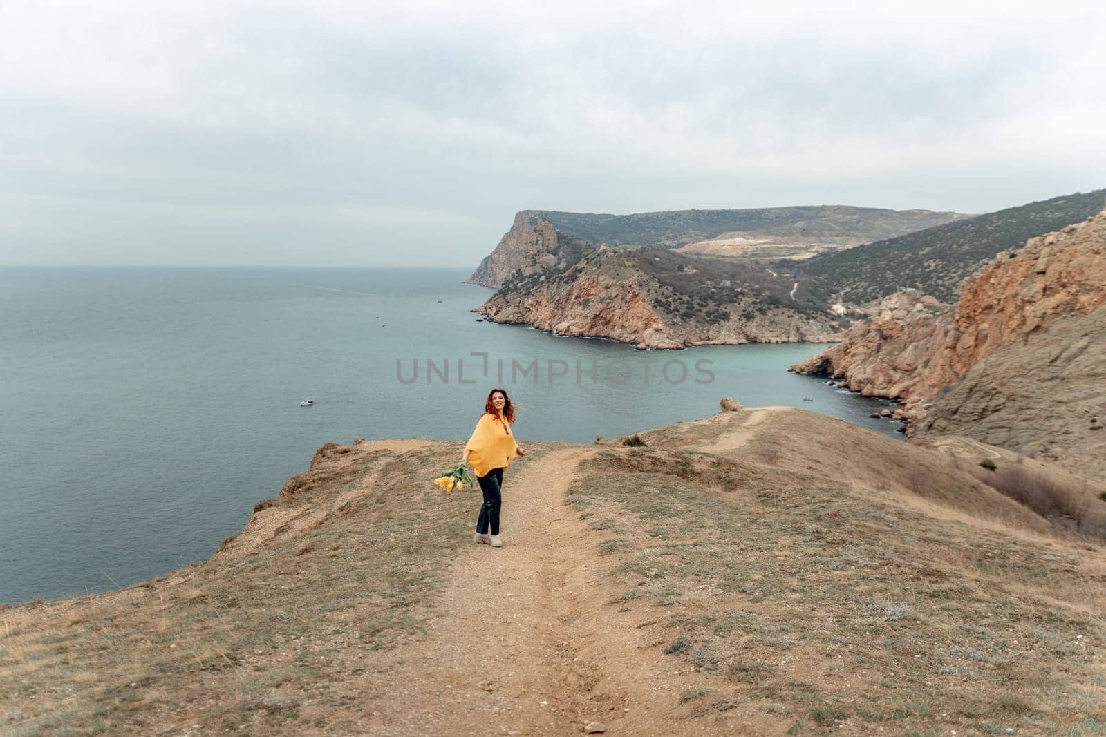 A woman is walking on a path near the ocean. She is carrying a bouquet of flowers