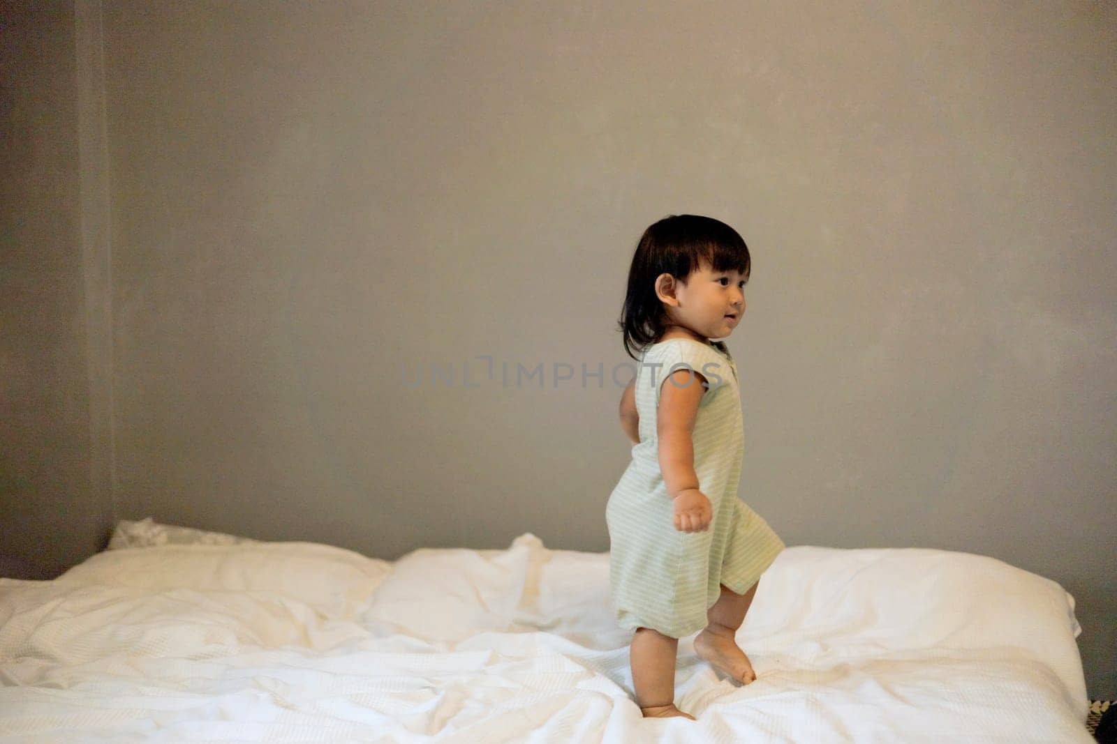 Child playing in bed in gray bedroom. Little Boy is Jumping On The Bed.