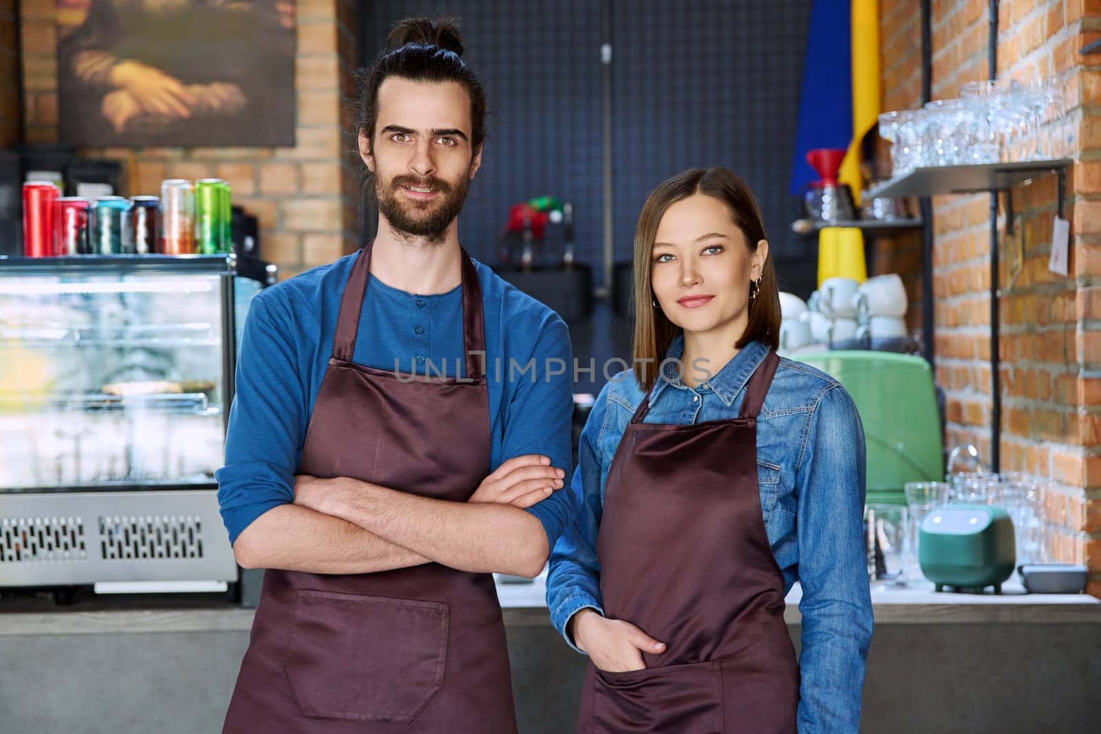 Small business team portrait of confident successful colleagues partners young man woman in aprons posing looking at camera at workplace in restaurant coffee shop cafeteria. Partnership teamwork work