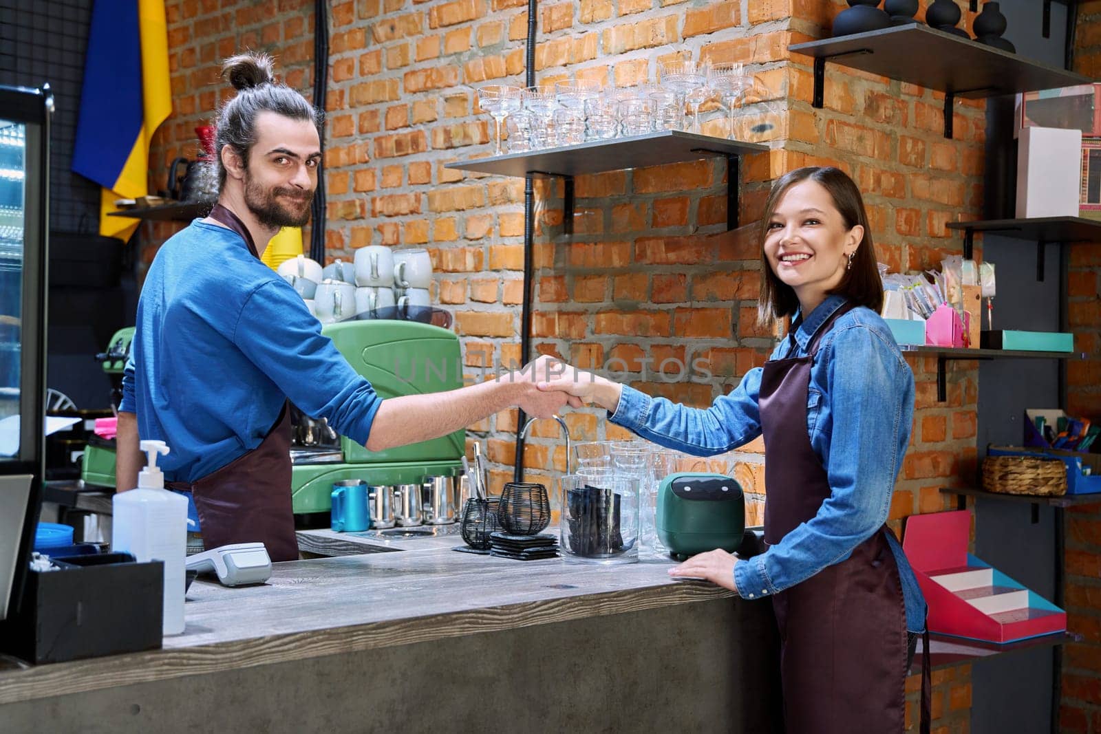 Colleagues, partners, young men and women in aprons shake hands in restaurant cafeteria coffee pastry shop. Cooperation, small business, partnership, teamwork, team, staff, friendship, success concept