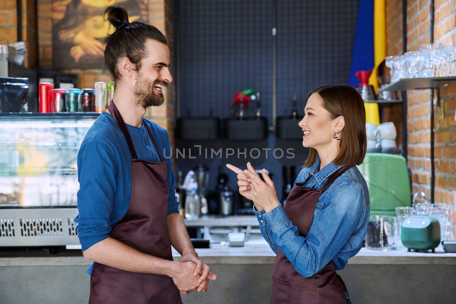 Colleagues business partners young man and woman in aprons talking at workplace by VH-studio