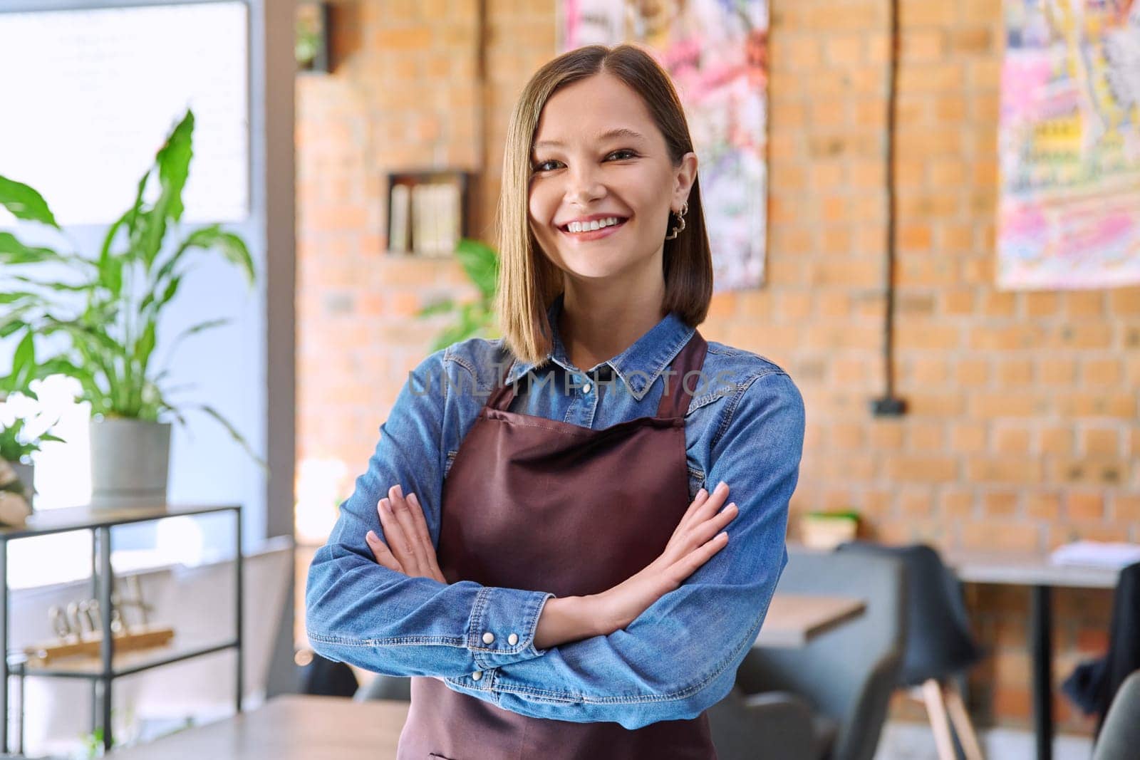 Young woman worker, owner in apron looking at camera in restaurant, coffee shop by VH-studio