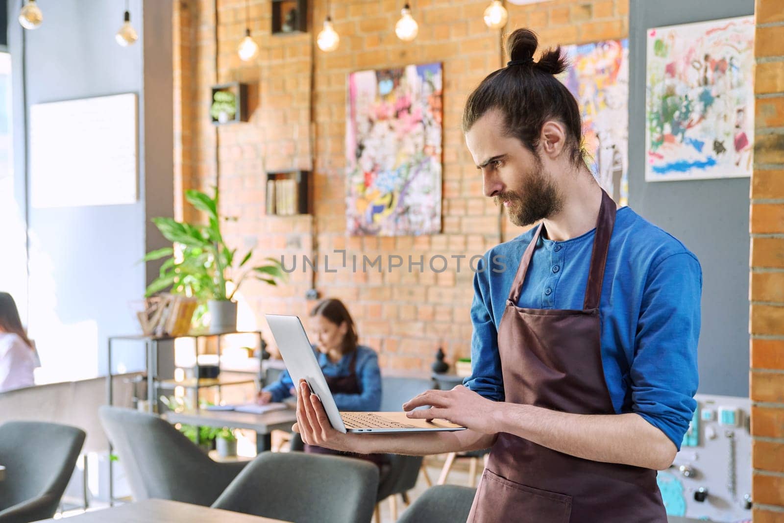 Man service worker owner in apron using laptop in restaurant cafeteria interior by VH-studio
