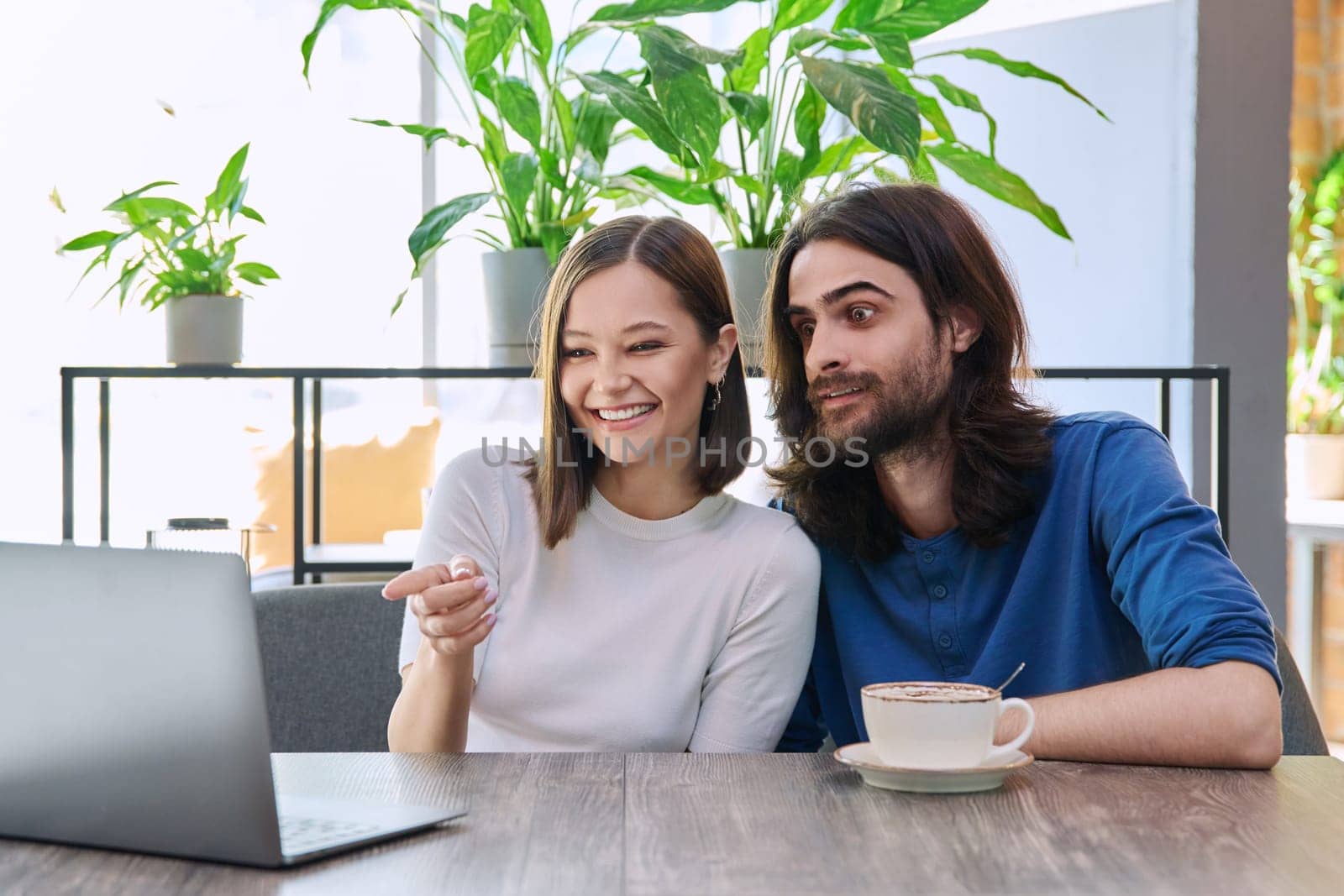 Happy smiling surprised young couple looking at laptop together while sitting in cafe, cafeteria. Leisure time for two, lifestyle, togetherness, relationship, communication, work study remotely