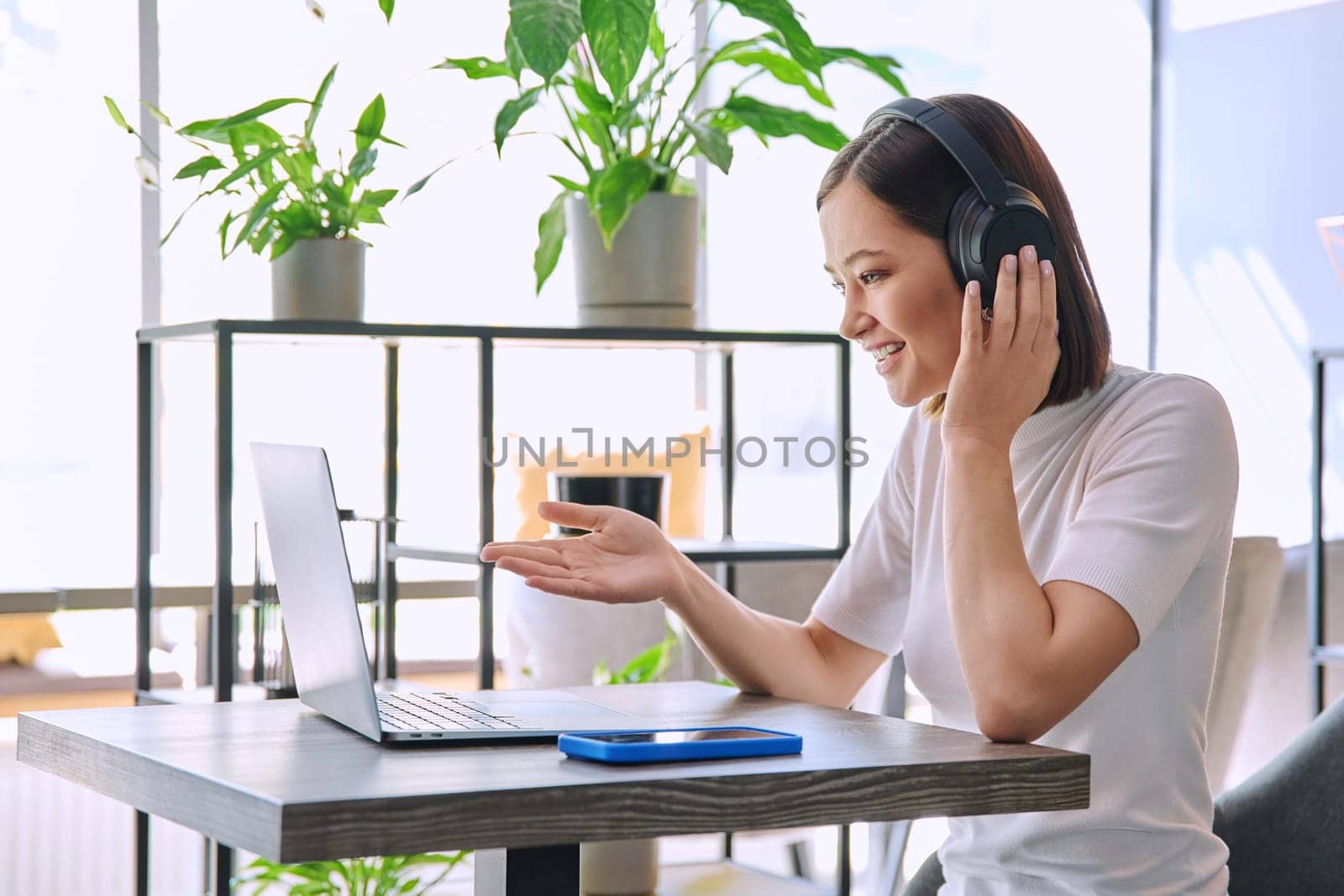 Young woman in headphones having work video chat conference call using laptop computer sitting in cafe coworking. Remote virtual online work study freelance blog vlog, internet technology youth concept