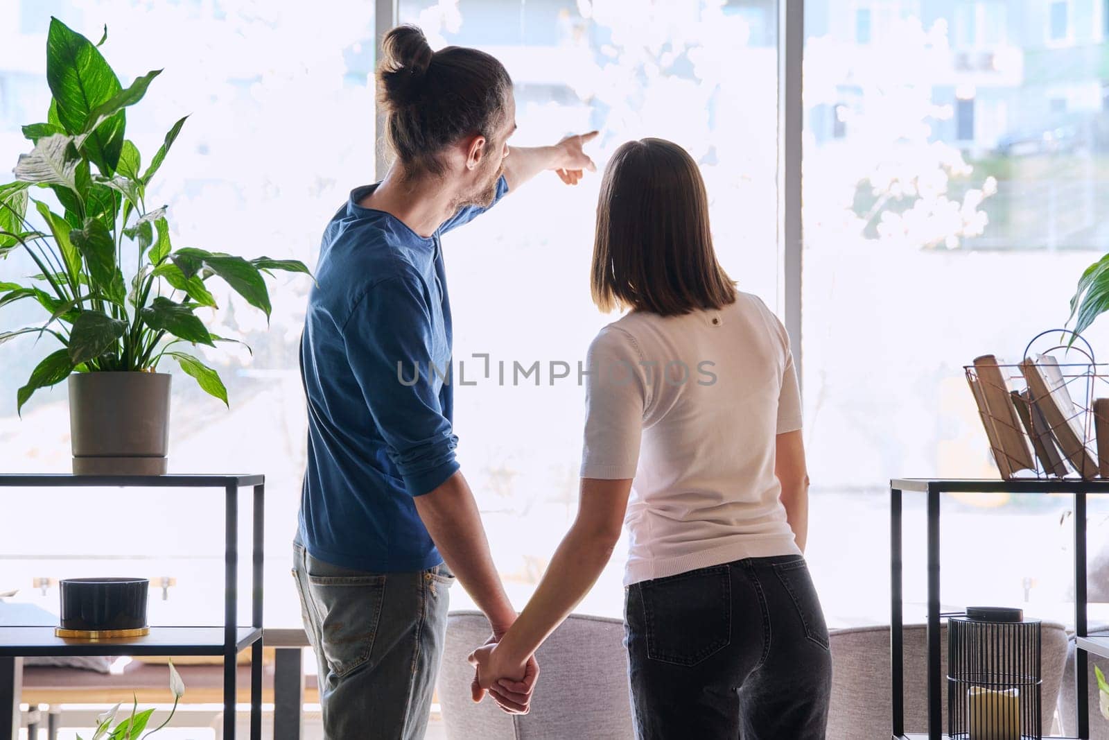 Back view, silhouette of young couple holding hands looking out window. Love friendship romance relationship, happiness, lifestyle, people concept