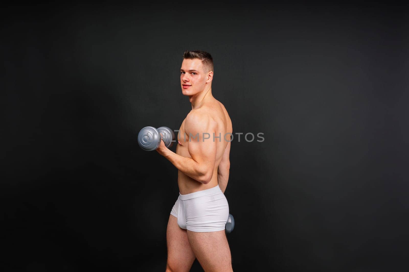 Man with pumped-up body with dumbbells in his hands white panties exercise