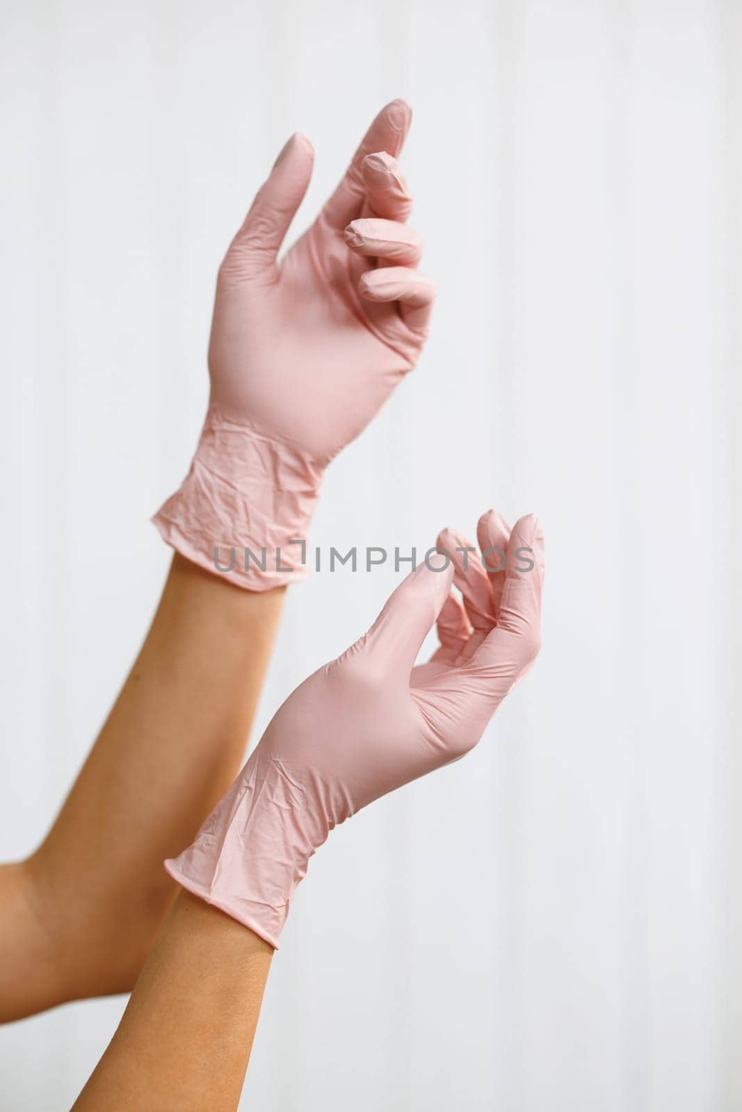Two hands of a woman wearing gloves on a white background. Prevention of viral diseases. Hands wearing a pink latex glove.