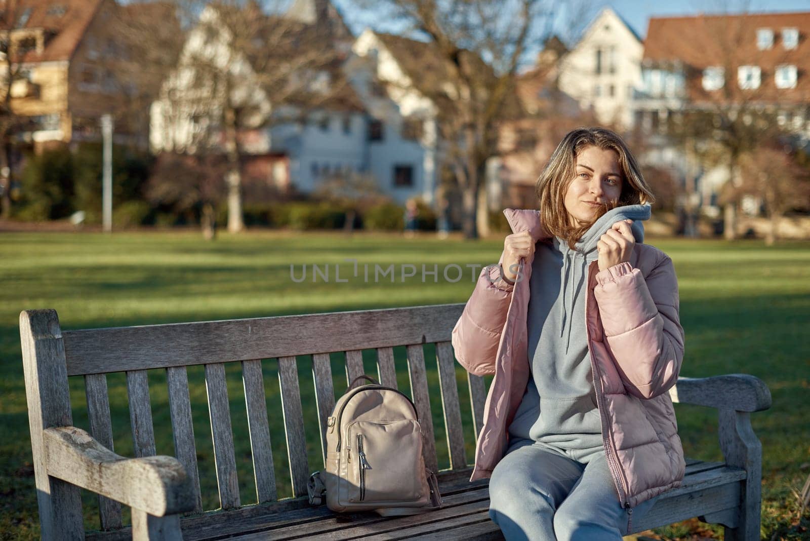 Winter Joy in Bitigheim-Bissingen: Beautiful Girl in Pink Jacket Sitting Amidst Half-Timbered Charm. beautiful girl in a pink winter jacket sitting on a bench in a park, set against the backdrop of the historic town of Bitigheim-Bissingen, Baden-Wurttemberg, Germany. by Andrii_Ko