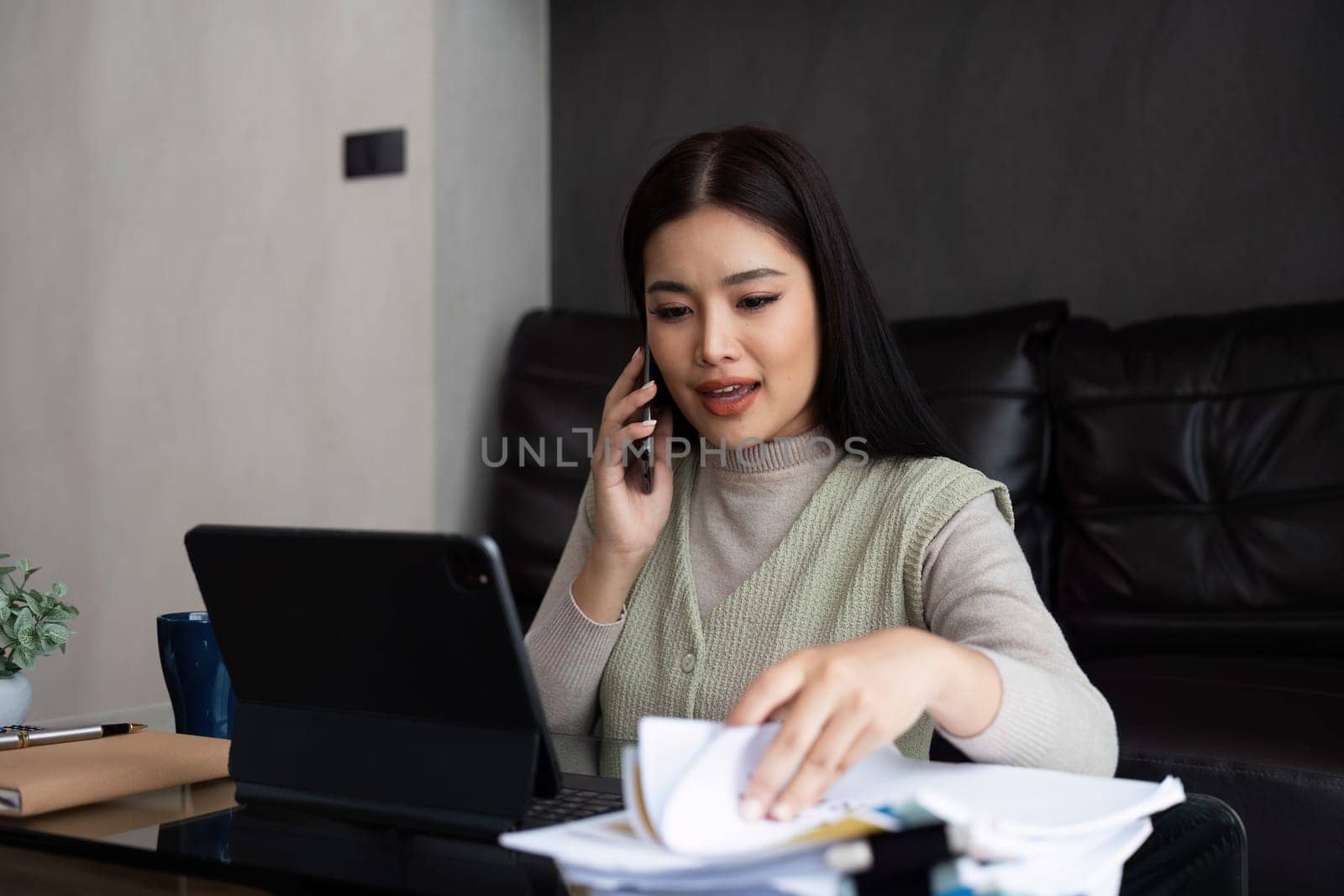 Asian business woman talking on mobile and working on laptop remotely from home. work from home concept by itchaznong