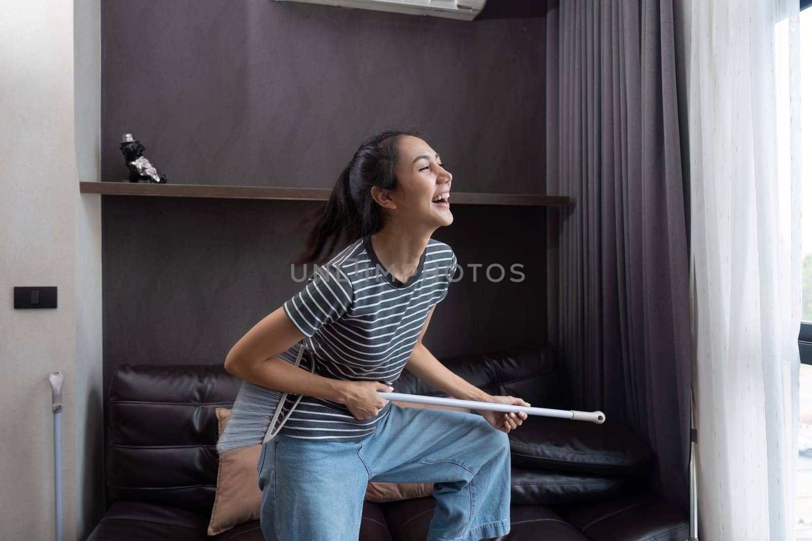 young asian woman having fun during cleaning, fooling with mop and broom.
