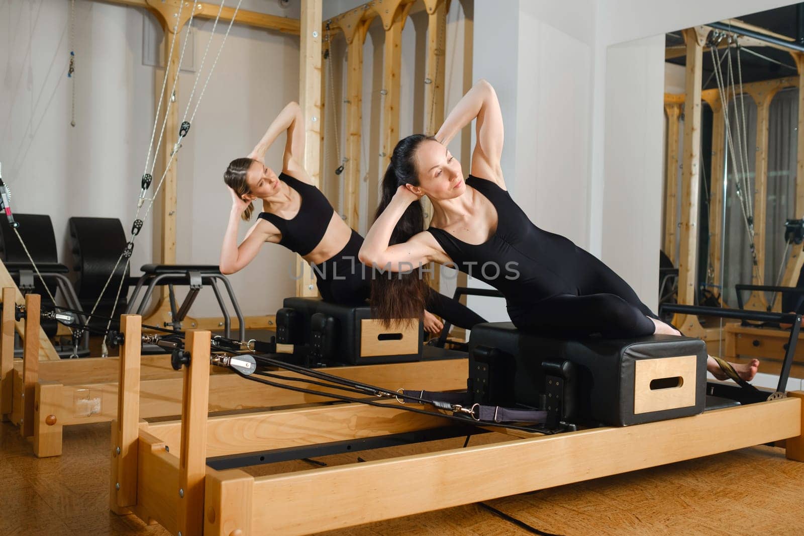 Two women balance on a pilates reformer machine in the gym by Lobachad