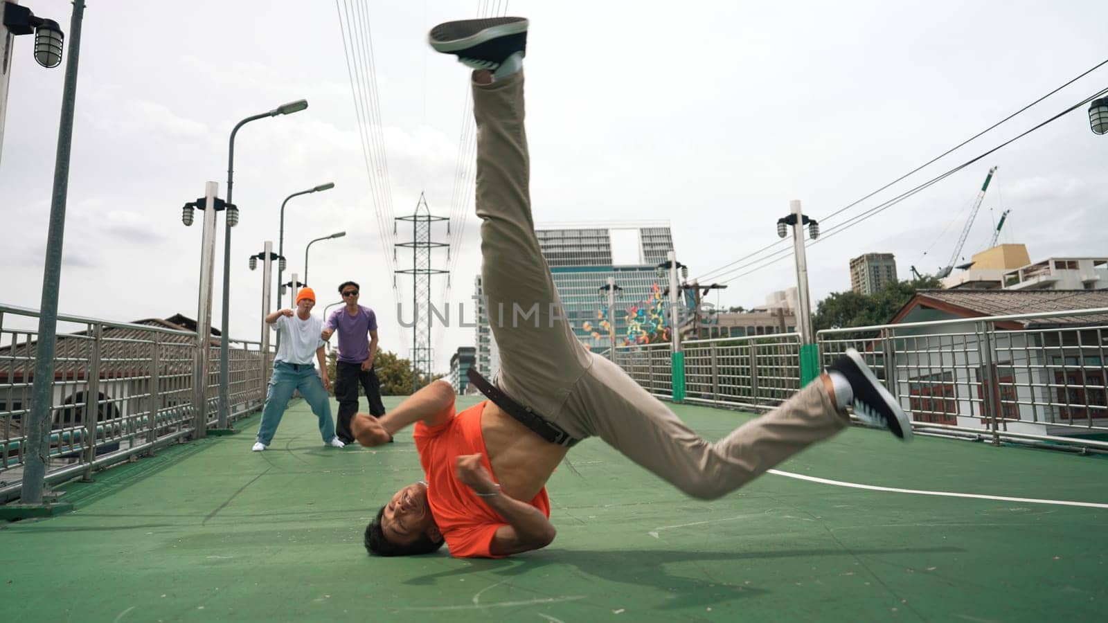 Young happy hipster perform break dancing or foot step with friend moving to hiphop music together. Skilled dancer doing freeze pose and waving hand. Modern lifestyle. Outdoor music 2024. Sprightly.