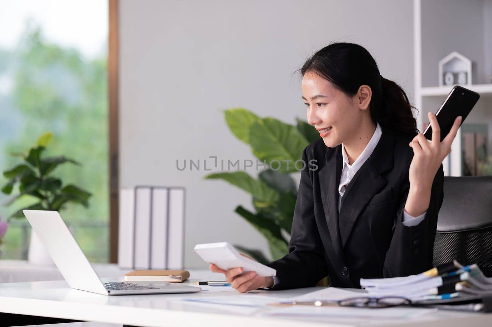 Beautiful accountant talking on the phone and calculating financial figures and calculating taxes for the company. by wichayada