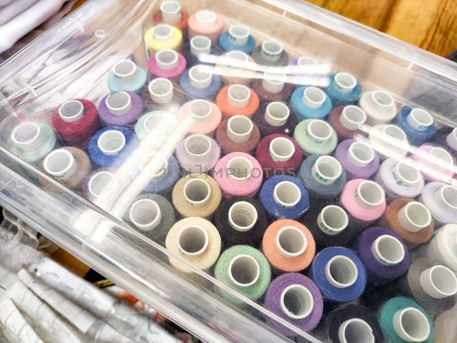 Vibrant Array of Thread Spools in Transparent Storage Box. Colorful thread spools neatly arranged in a clear plastic container