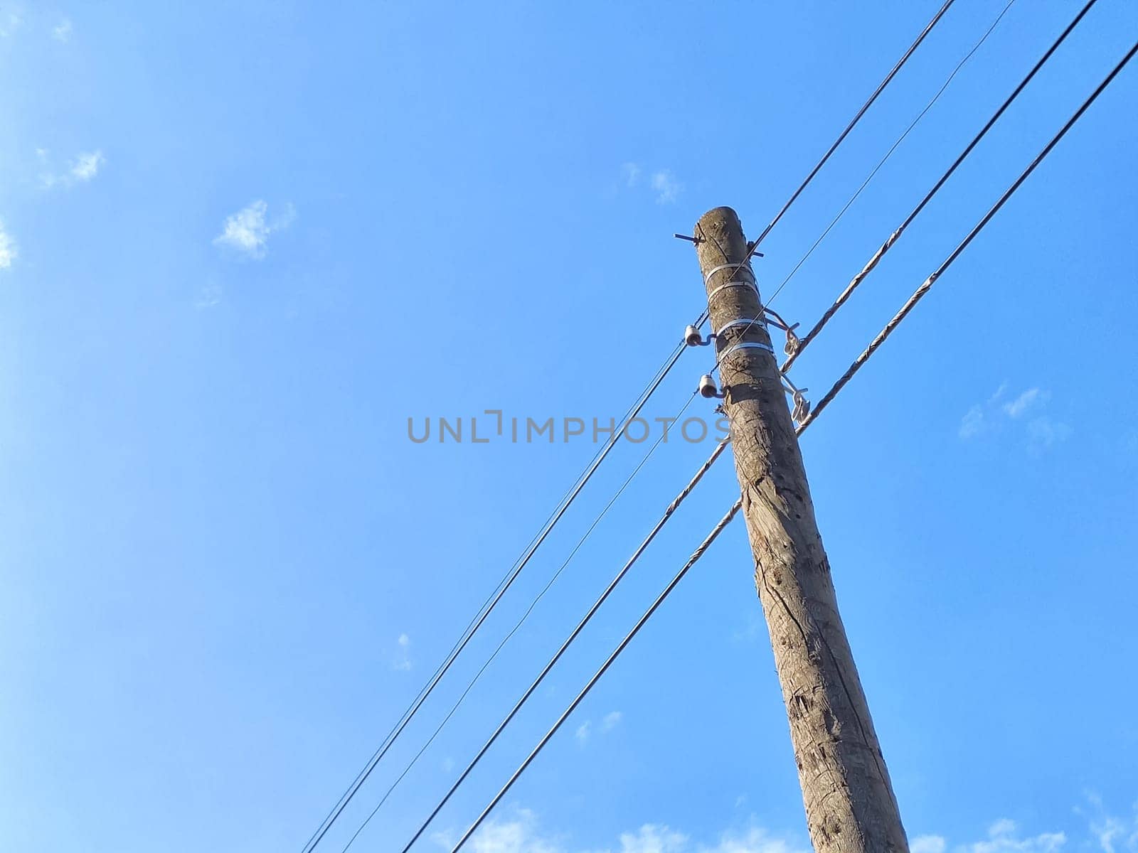Old power line pole against blue sky in sunny day by keleny