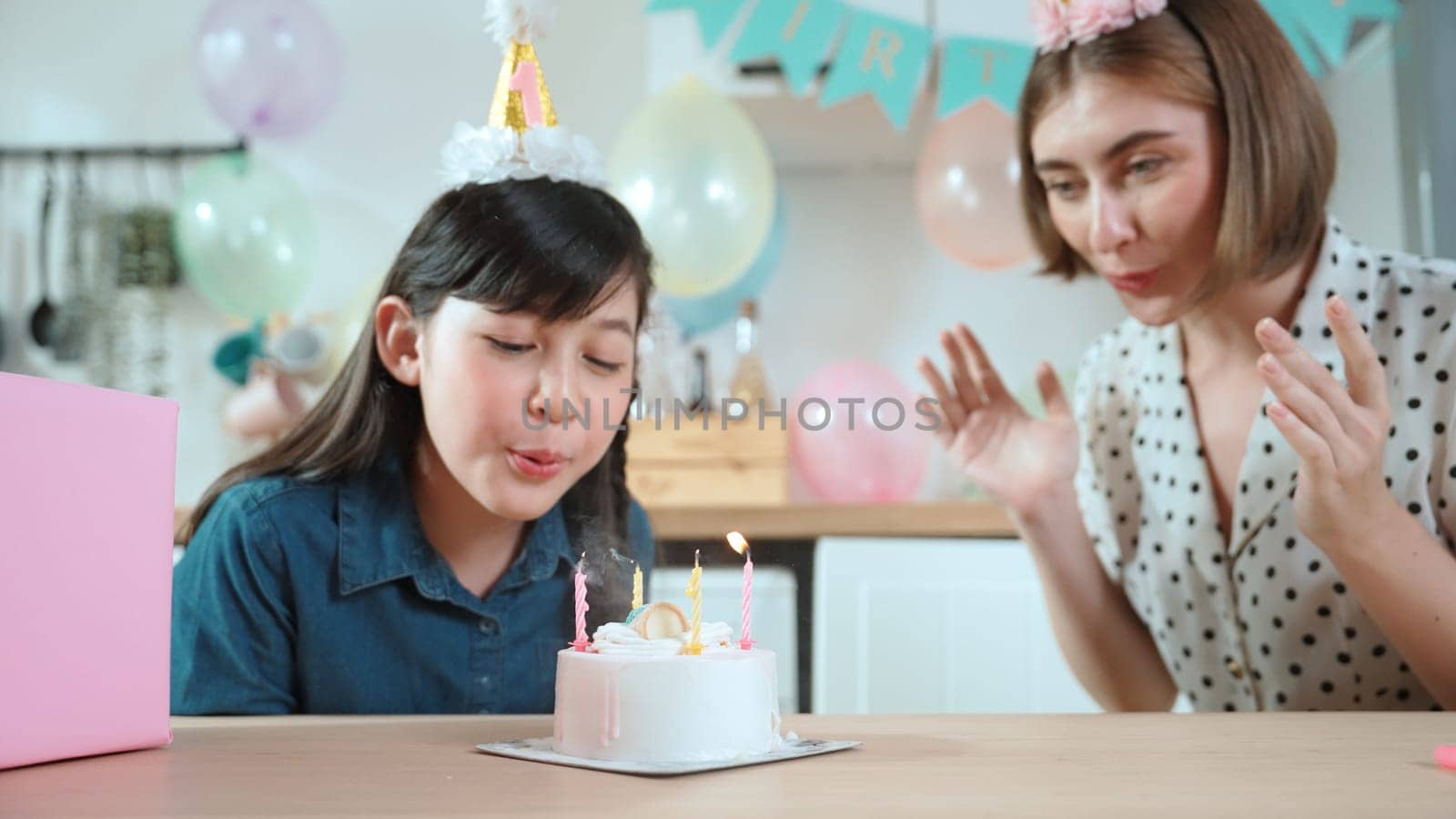 Happy cute child making a wish and blowing birthday cake candle surrounded by family wearing party hat celebrate in special occasion. Closeup of girl blow candle while family clapping hands. Pedagogy.
