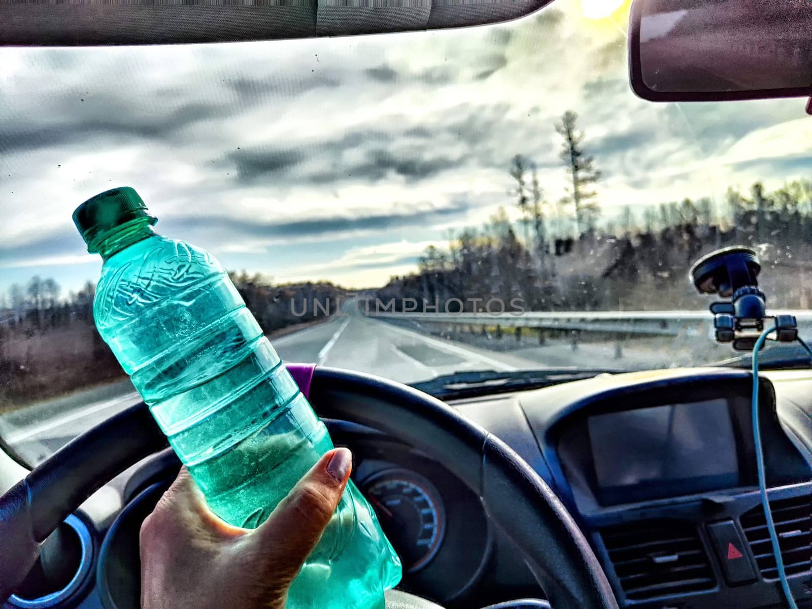 Driver Holding Water Bottle During Road Trip. Hand holding a water bottle in car with view of road. Ability to stay awake while driving for long time by keleny