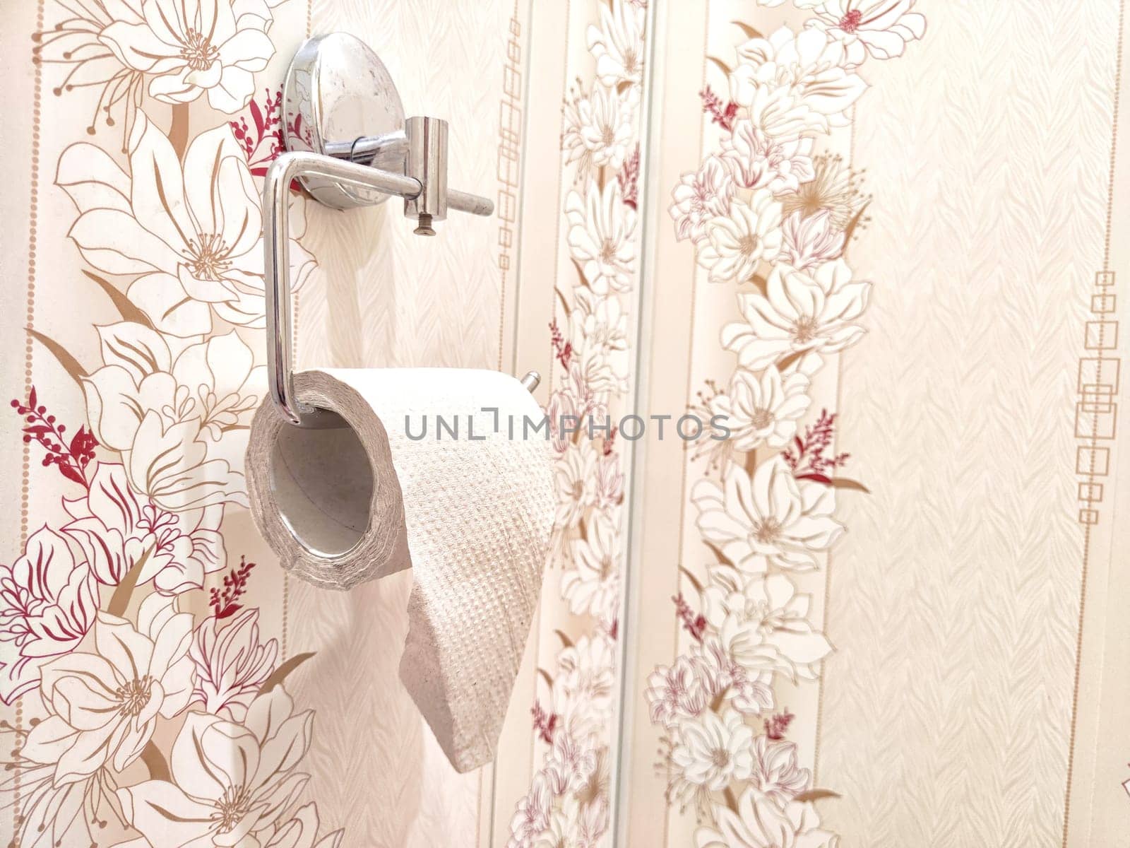 Toilet paper on a chrome holder against decorative floral wallpaper. Restroom Toilet Paper Holder With Floral Wallpaper by keleny