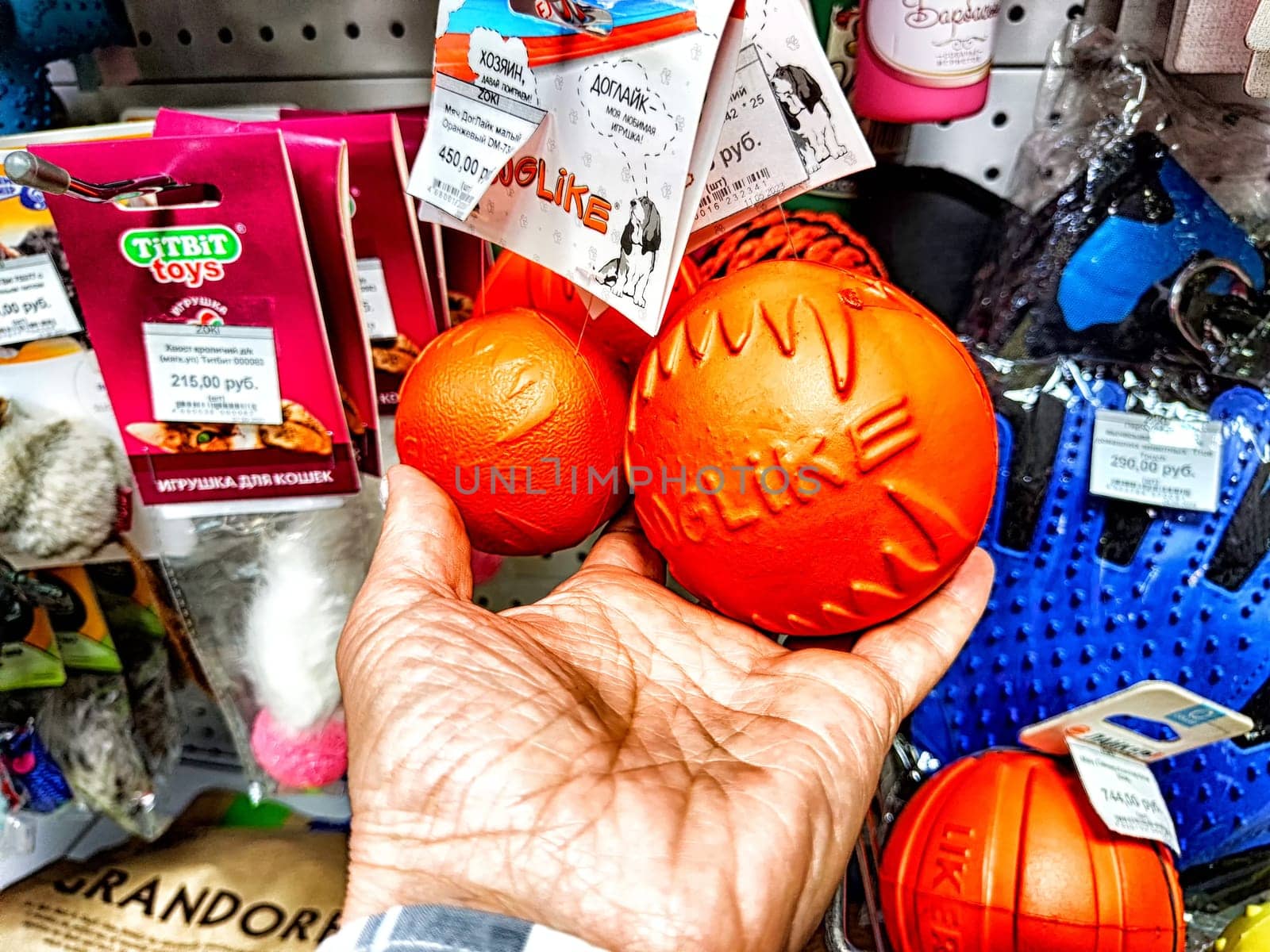 Kirov, Russia - September 08, 2023: Dog ball in hand among other things in the store. Persons hand selecting dog ball from an array of pet toys by keleny