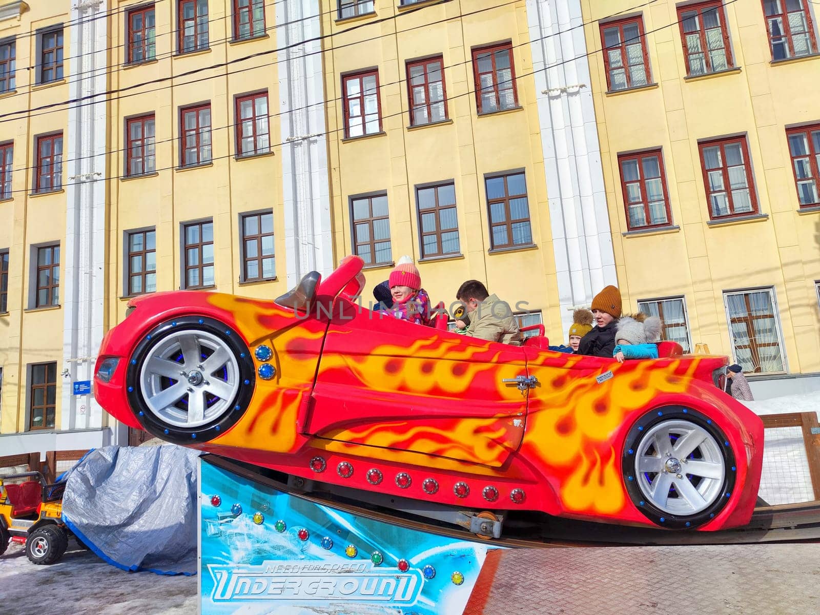 Kirov, Russia - March 17, 2024: People enjoy ride in whimsically designed flame-decorated carousel car. Amusement Ride Fun With Flaming Red Car