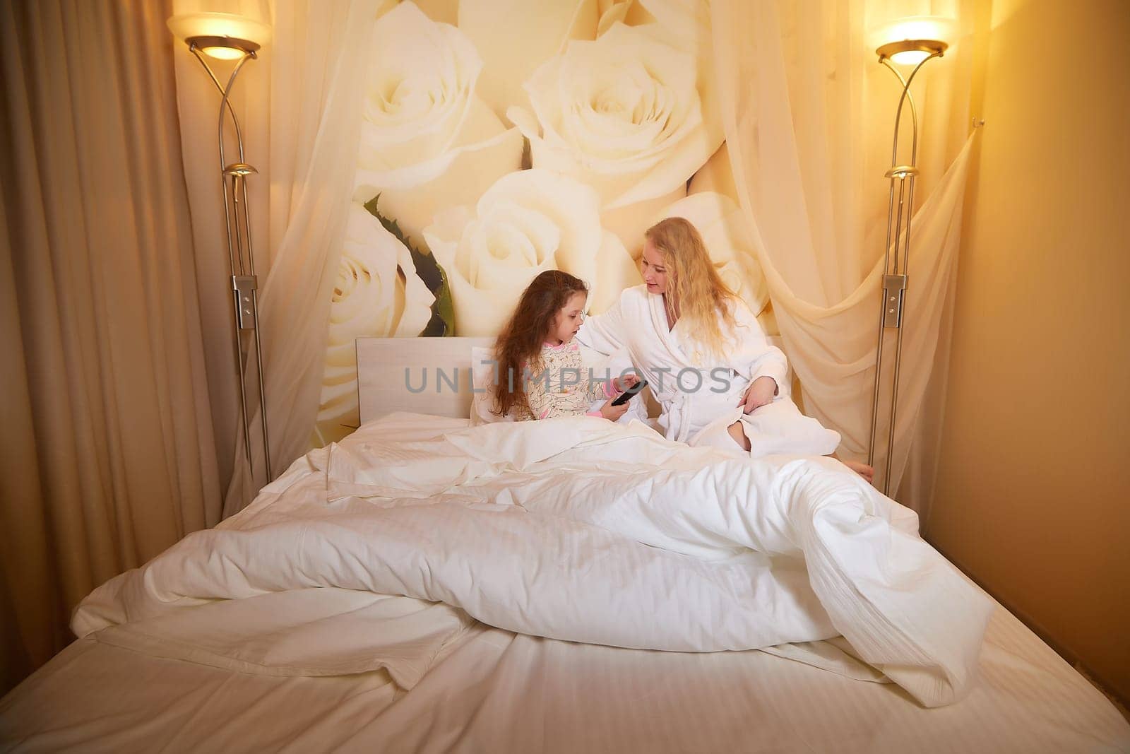 Mother and daughter happily relax, fun and conversation together on bed in bedroom. The concept of tenderness between mom and girl