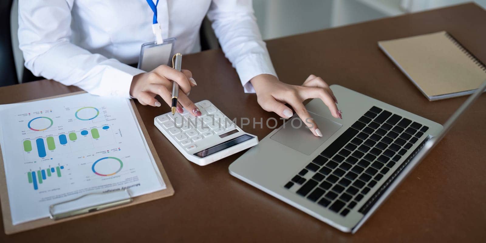 Finance concept. Close up businesswoman hold a graph pen and writing report, and memo, and analyzing business documents with a laptop computer by nateemee