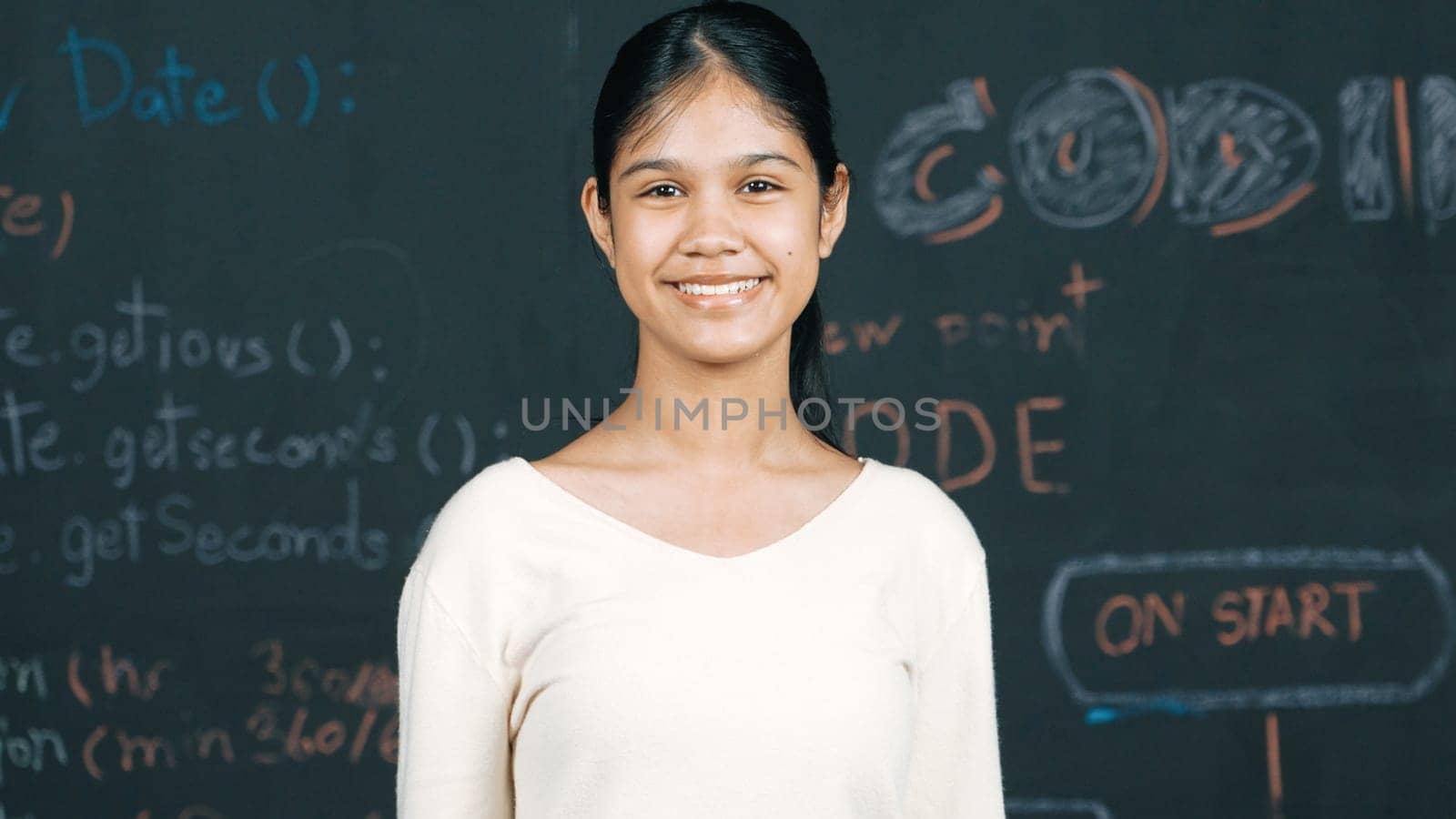 Caucasian woman looking at camera while standing at blackboard. Cute happy student smiling while stand in front of blackboard with engineering prompt or code in STEM technology class. Edification.