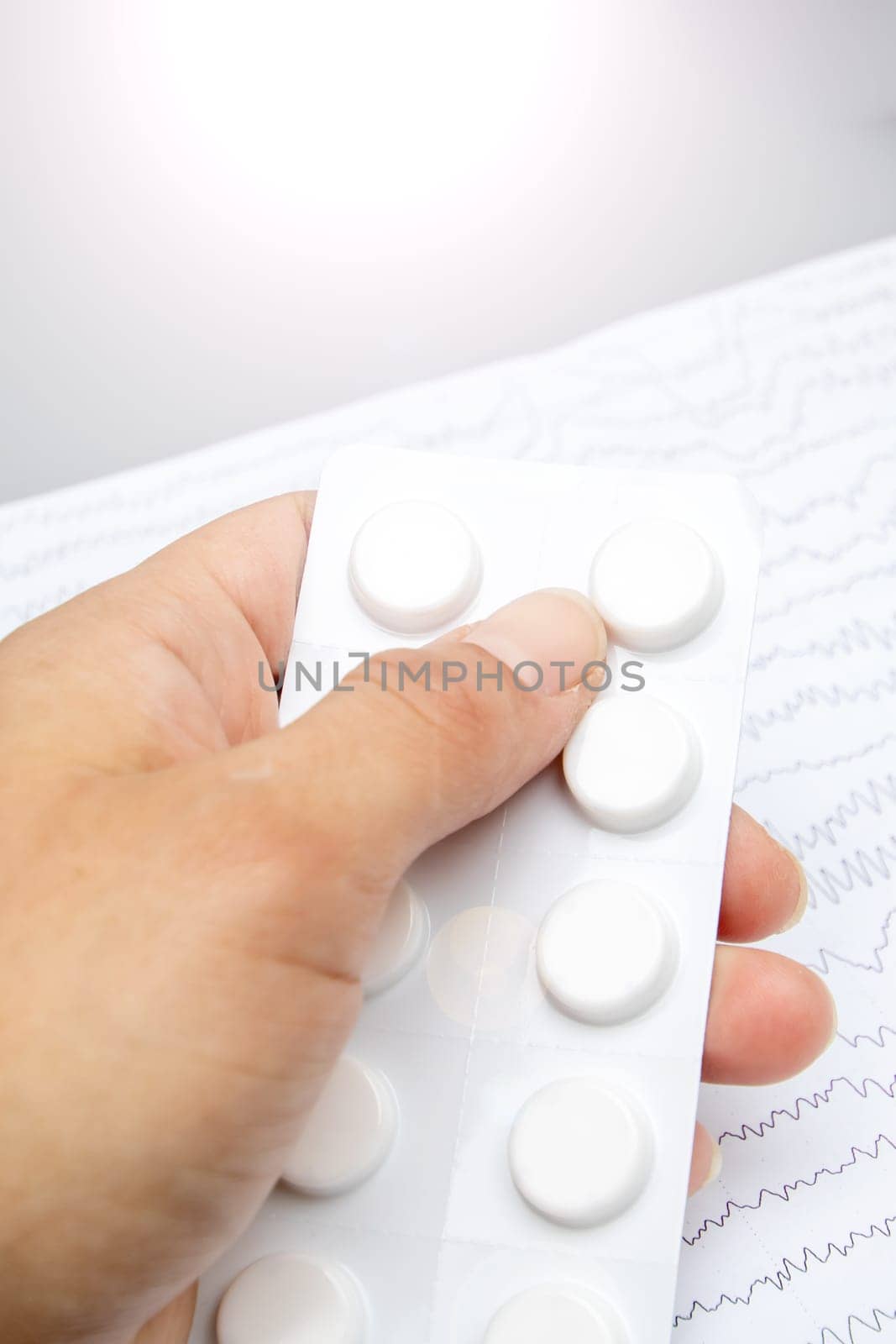 The person is holding a blister pack of pills in their thumb and finger by Vera1703