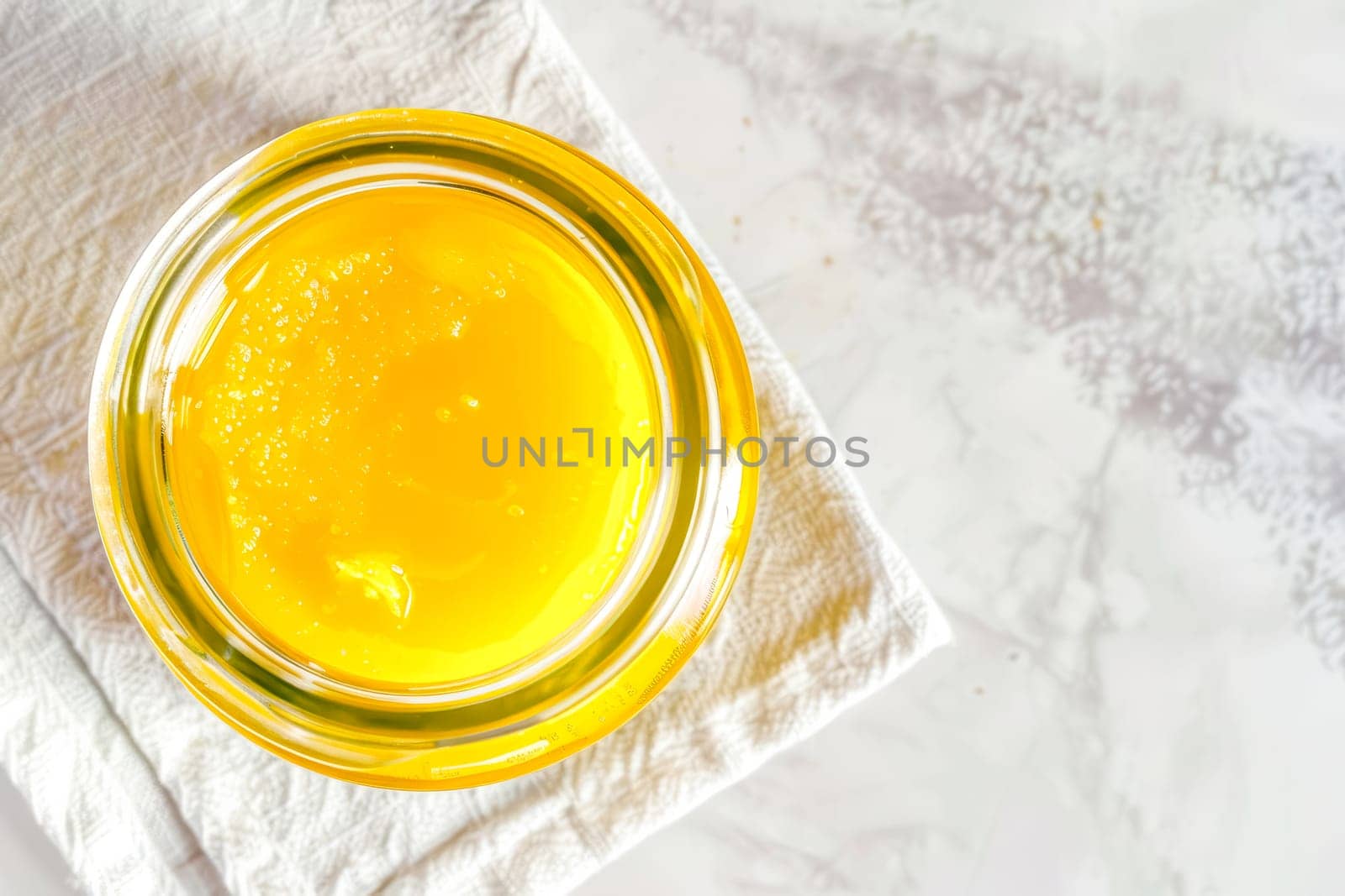 Top view, jar of ghee on a linen napkin with a spoon, light background.