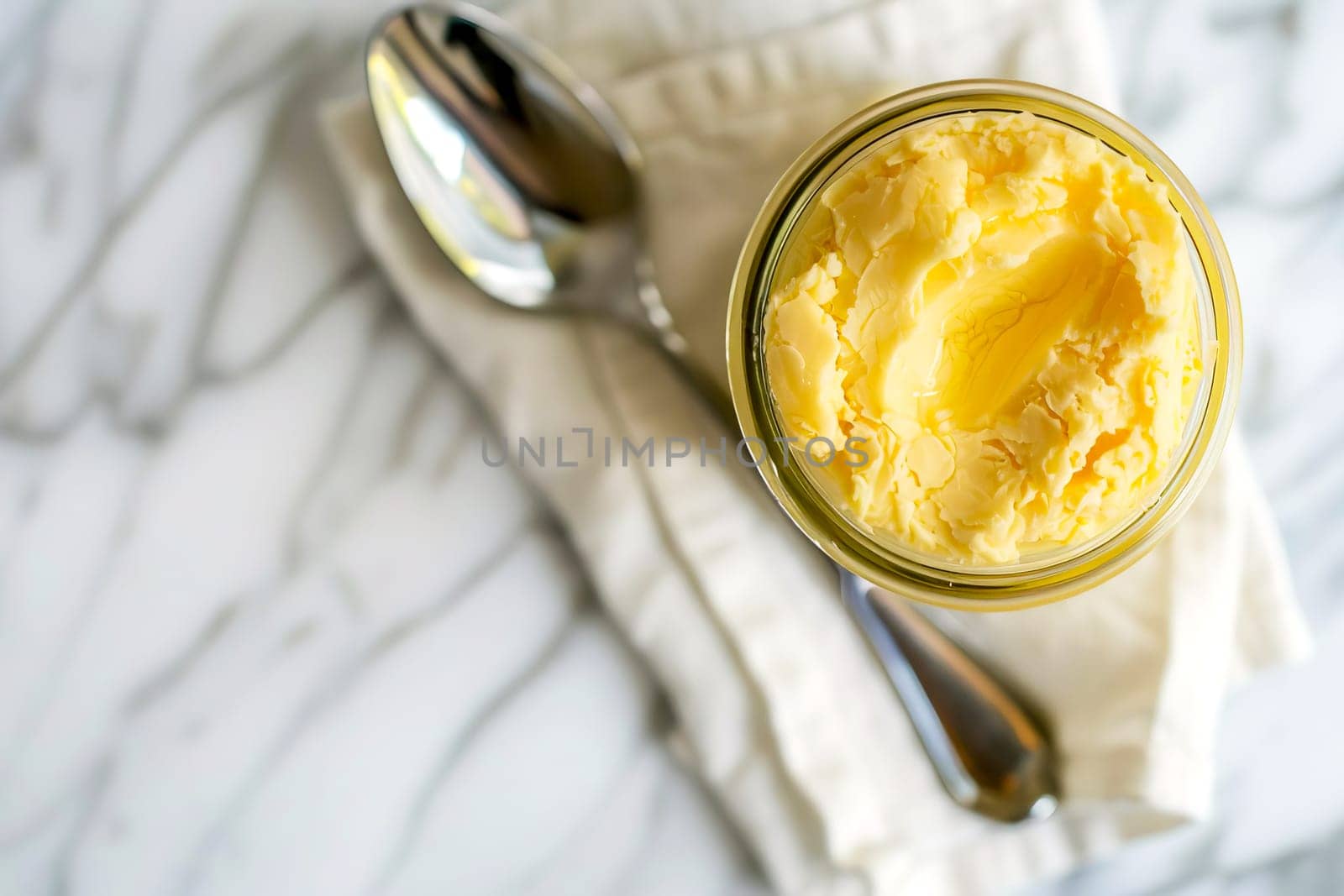 Top view, jar of ghee on a linen napkin with a spoon, light background.