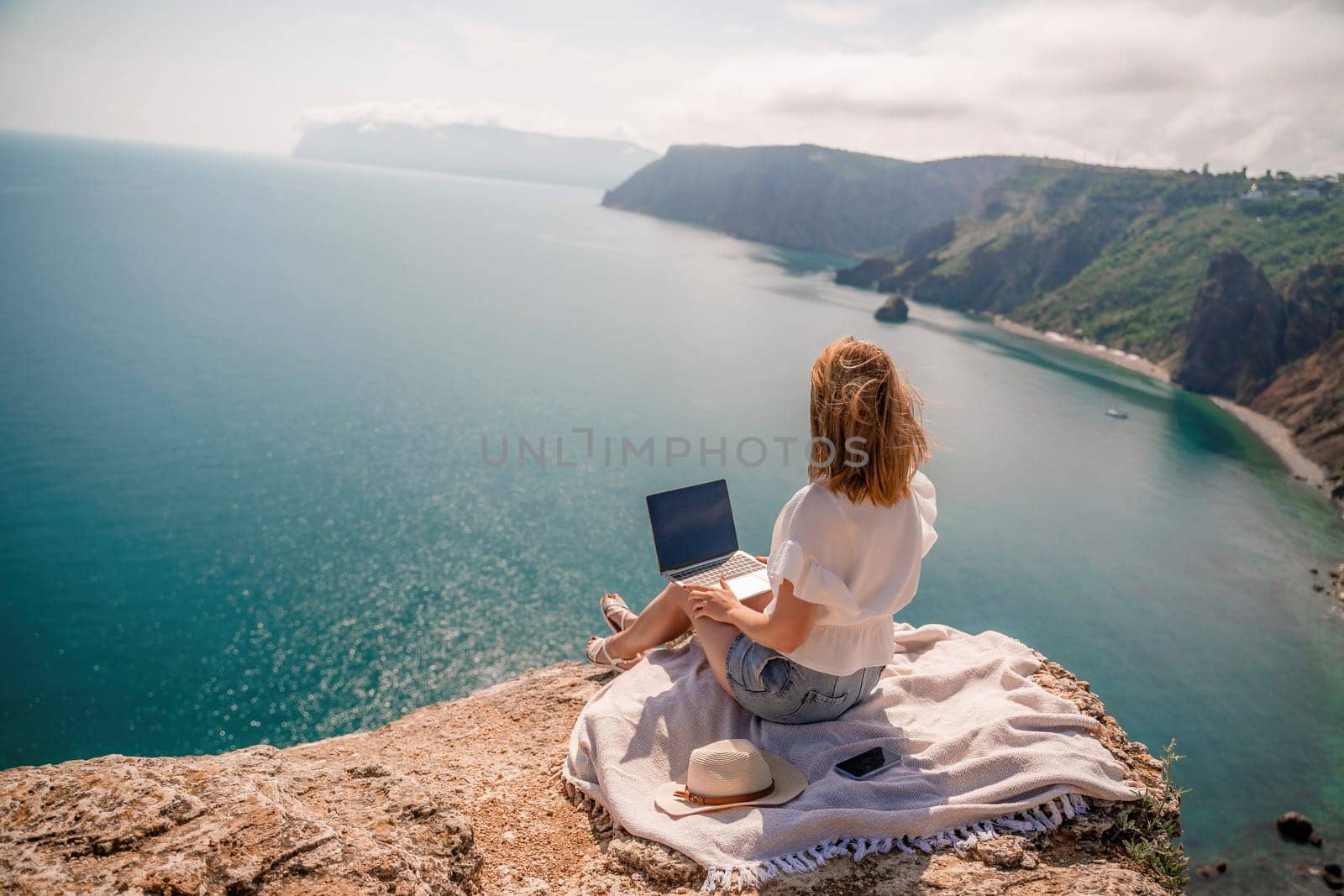 Freelance woman working on a laptop by the sea, typing away on the keyboard while enjoying the beautiful view, highlighting the idea of remote work